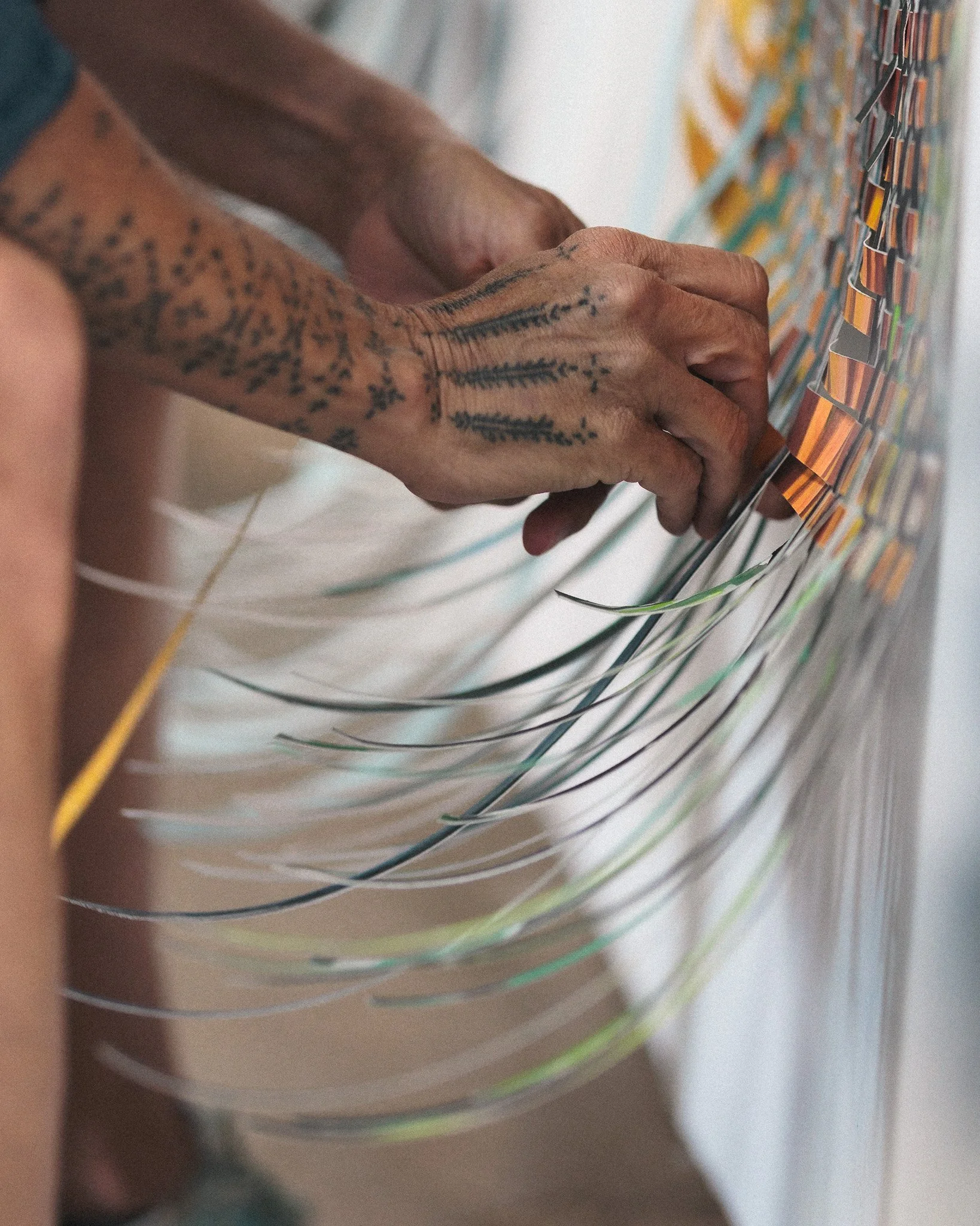 A person's tattooed arms reaching toward a wall filled with colorful sticky notes or cards arranged in rows.