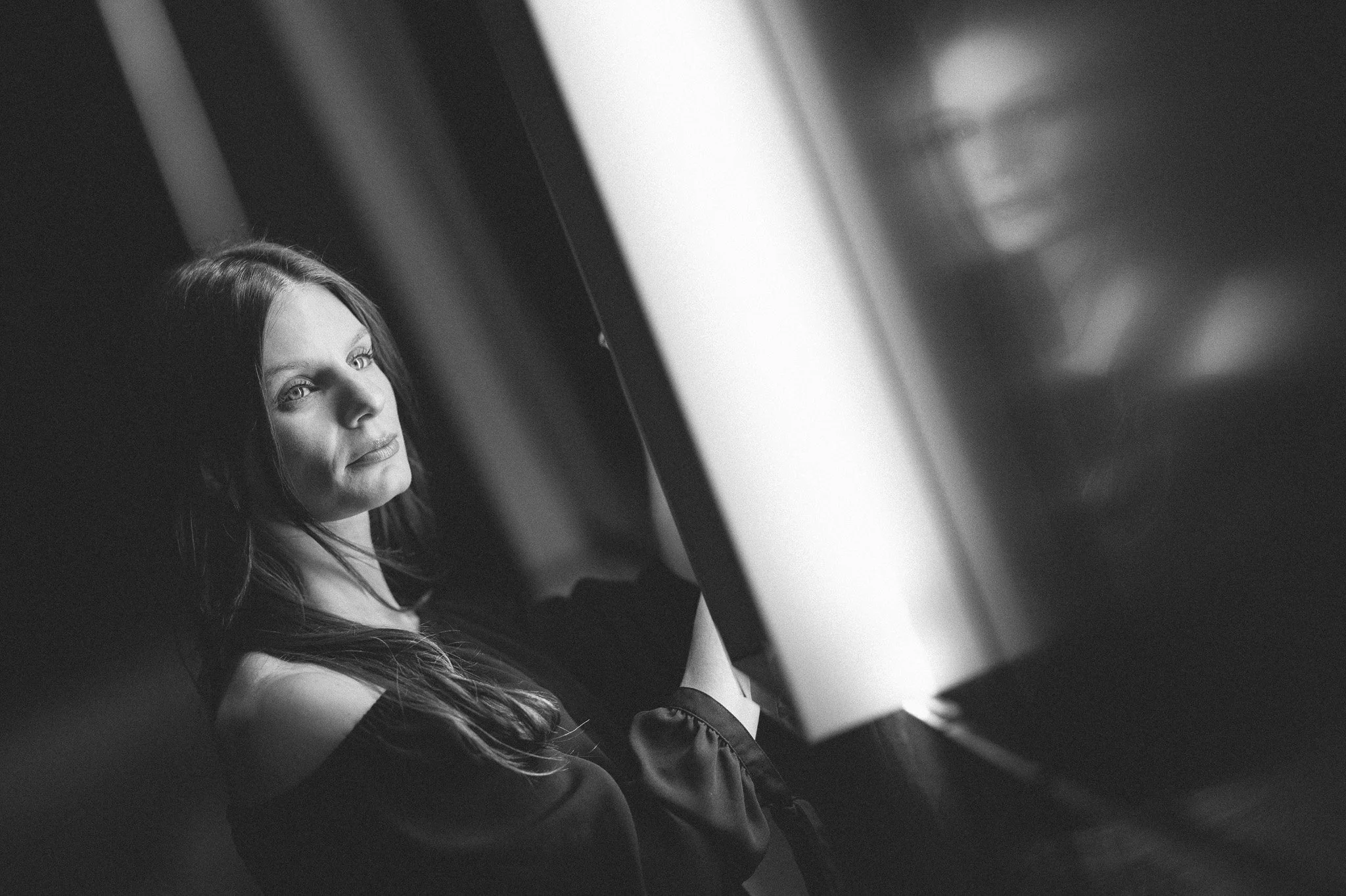 A woman with long hair looking into a mirror, reflected face visible, in black and white.