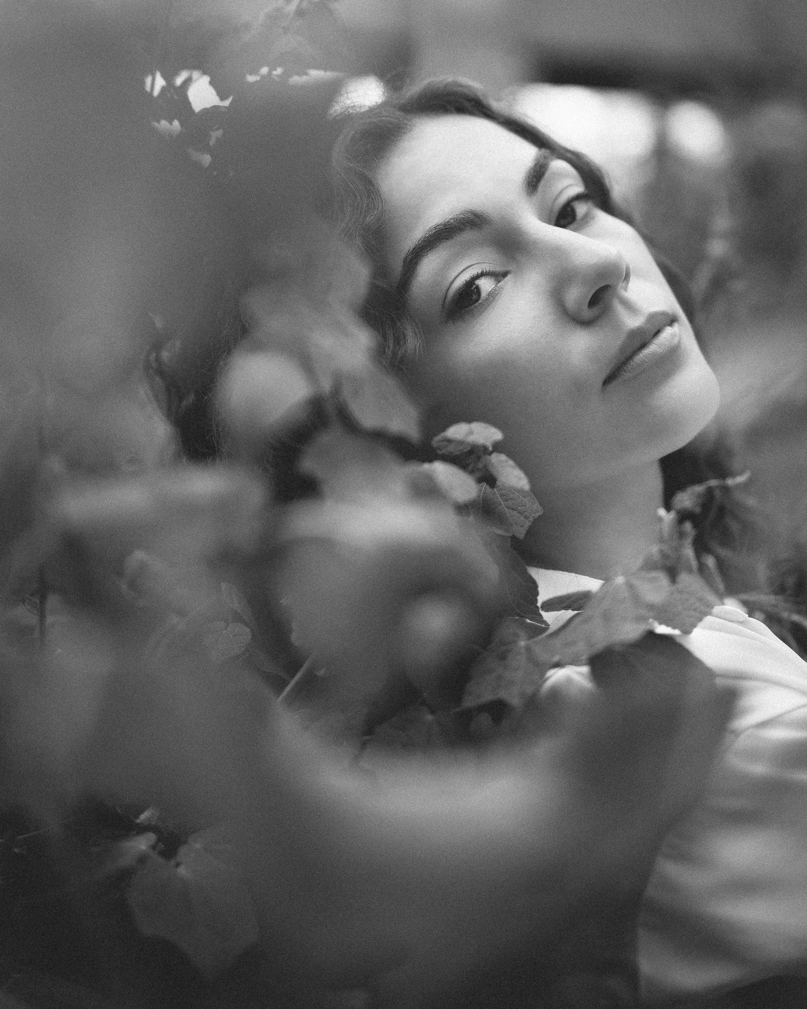 Black and white close-up photo of a woman with dark hair, closed eyes, and full lips, surrounded by floral elements.