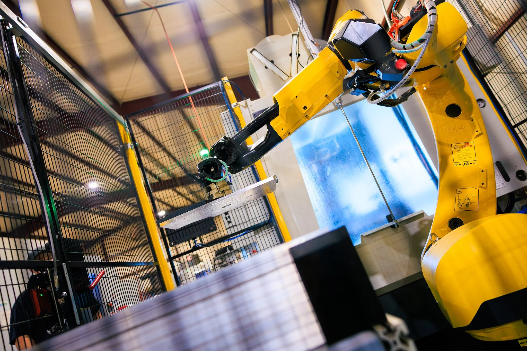 A yellow industrial robotic arm operating inside a fenced workspace.