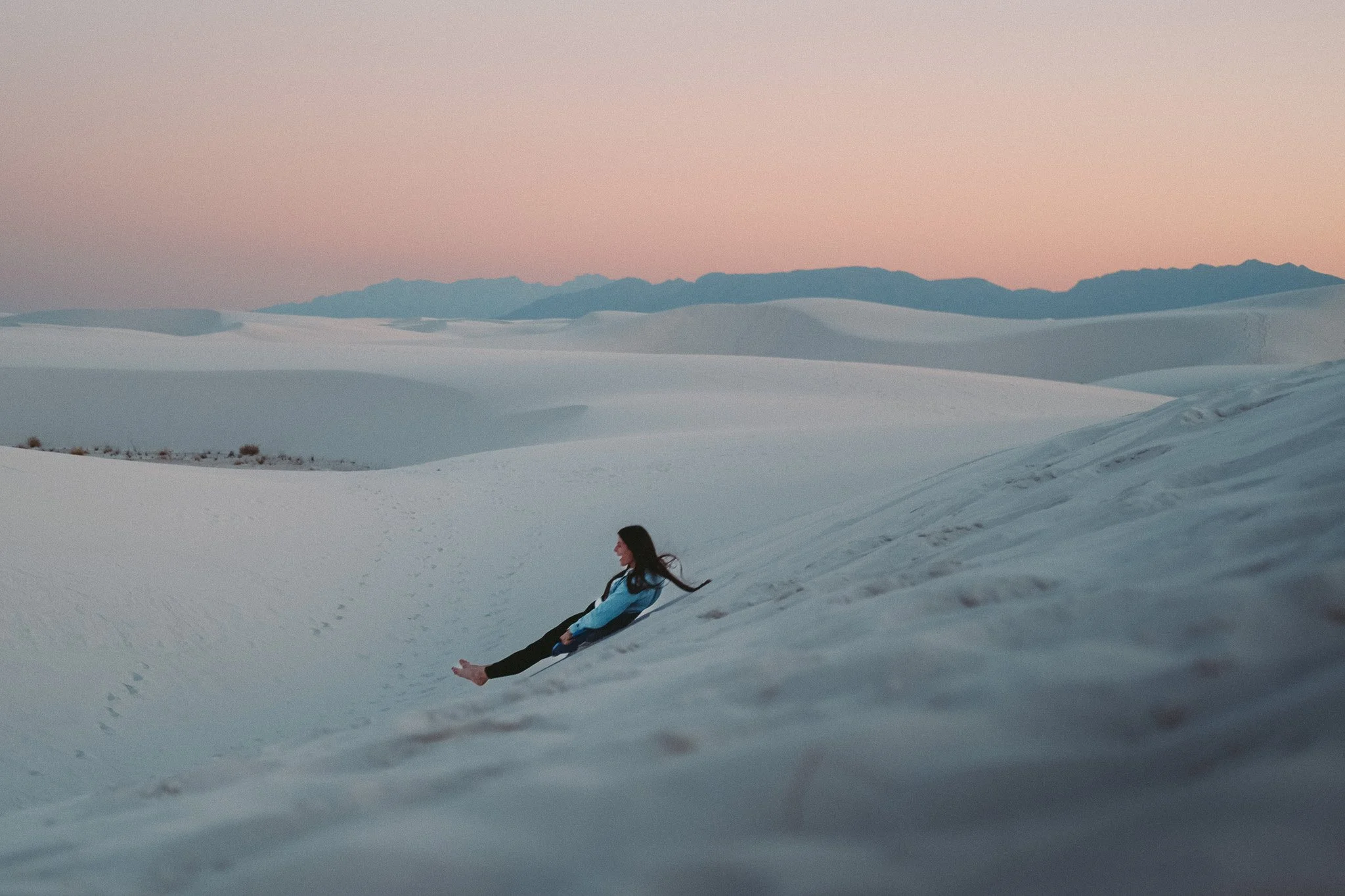 A person sitting in the snow in a snowy landscape with mountains in the background, at sunset or sunrise.
