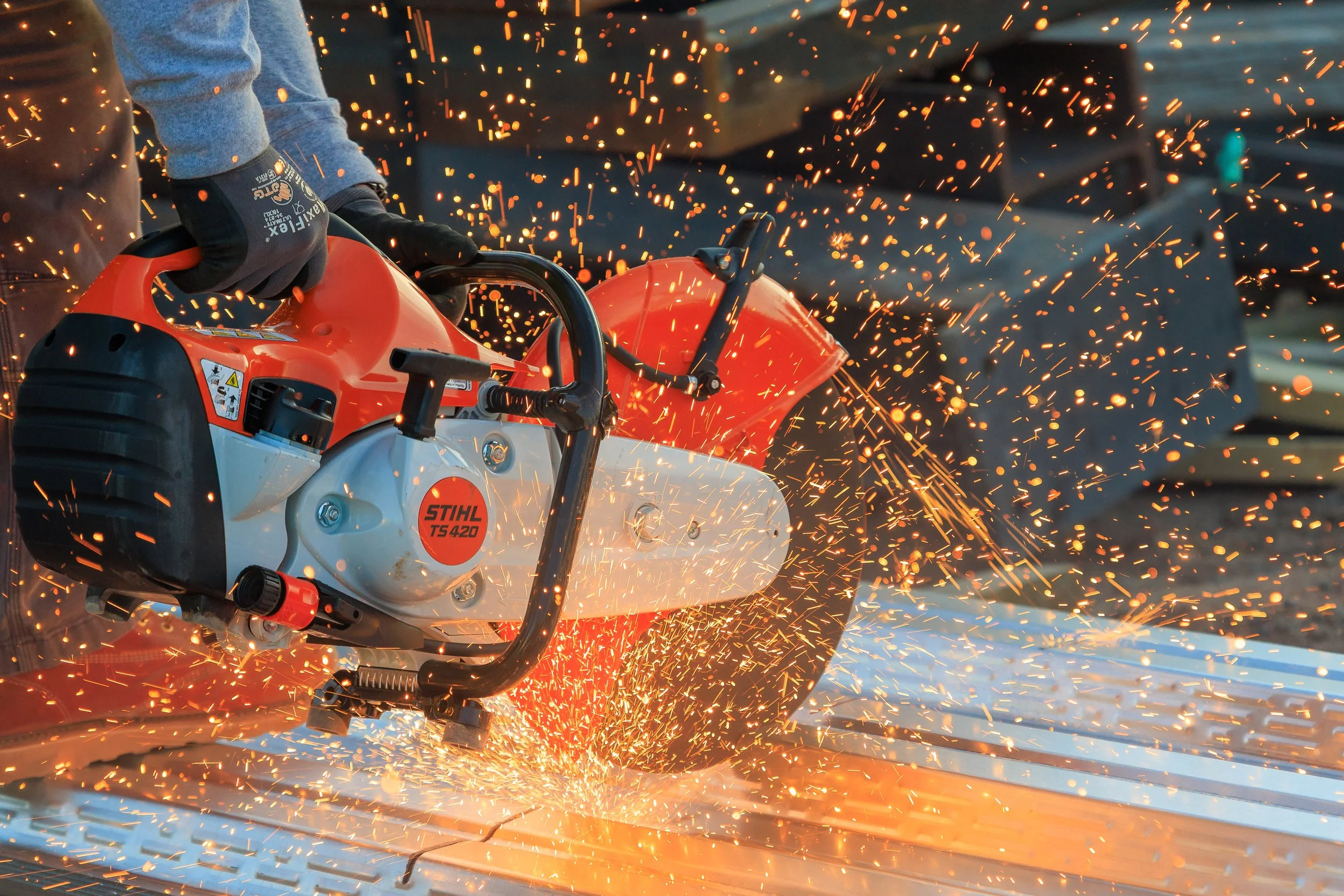 Person wearing gloves using a chainsaw to cut through metal, sparks flying from the cutting process.