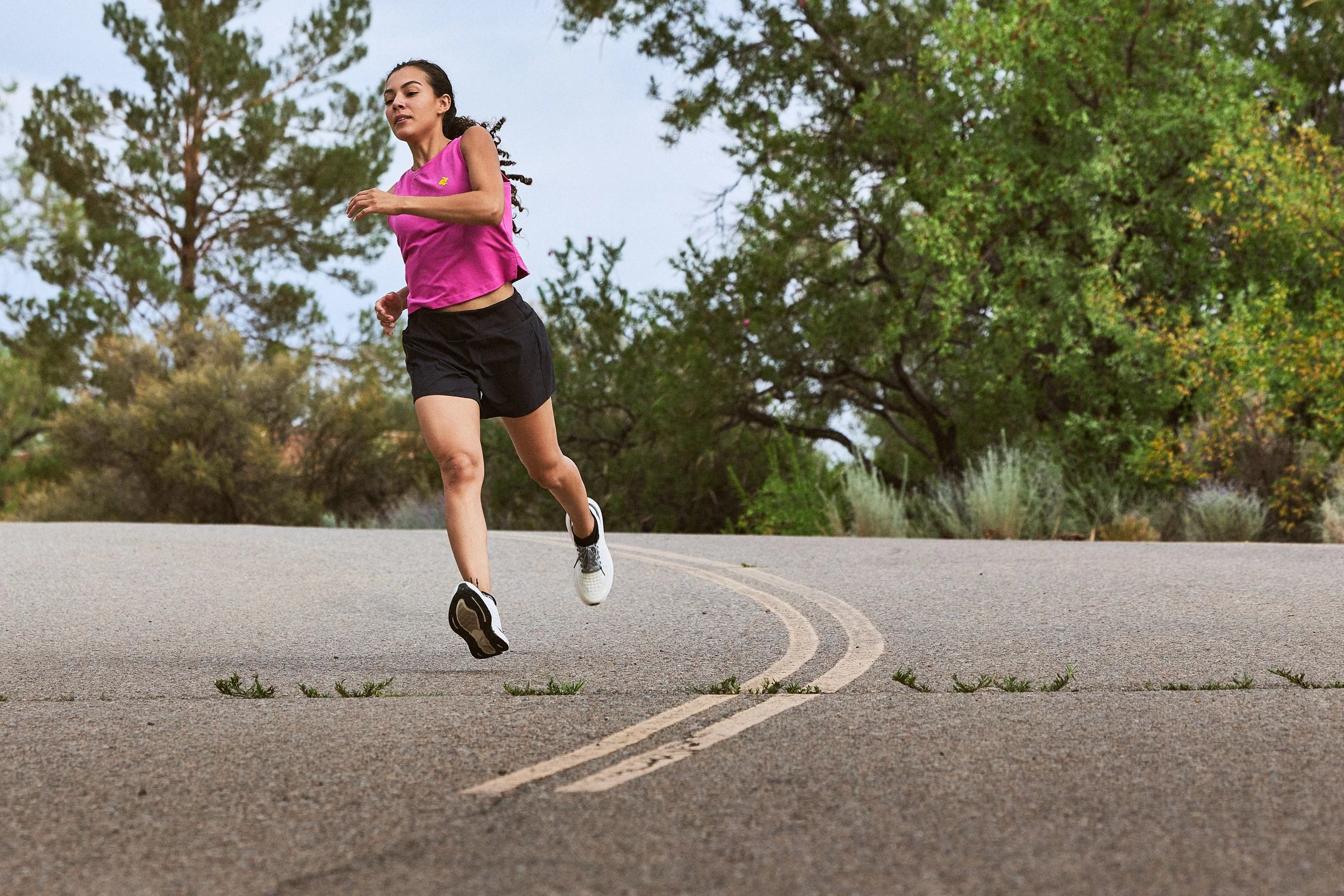 A woman jogging on a paved road surrounded by trees and greenery during daytime.