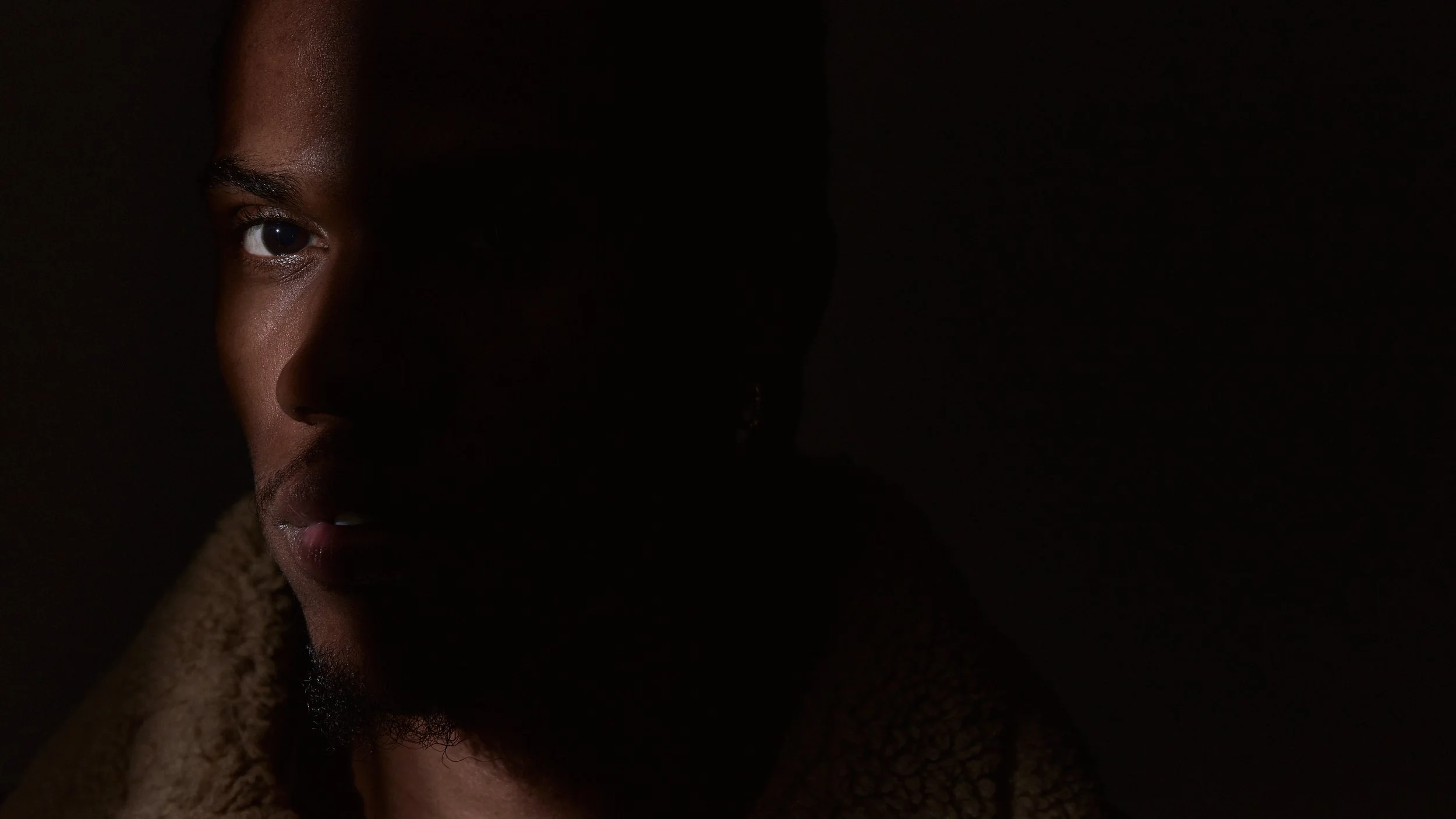 A close-up of a woman's face half in shadow, showing one eye and part of her nose and lips in low light.