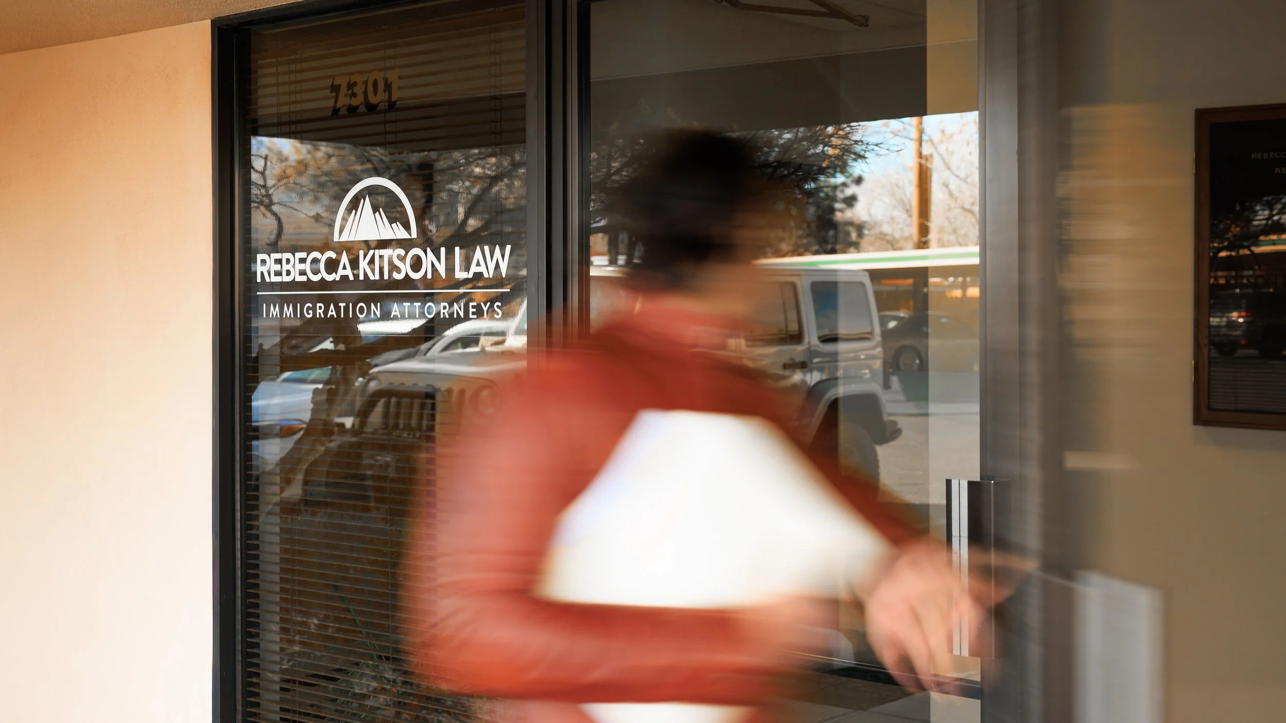  storefront window with the sign 'Rebecca Kitson Law, Immigration Attorneys' and a person walking past.