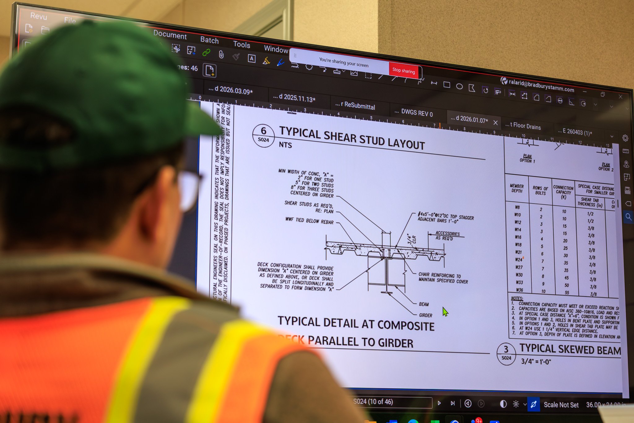 A person wearing safety gear looking at a computer monitor displaying a technical engineering drawing titled 'Typical Shear Stud Layout.'