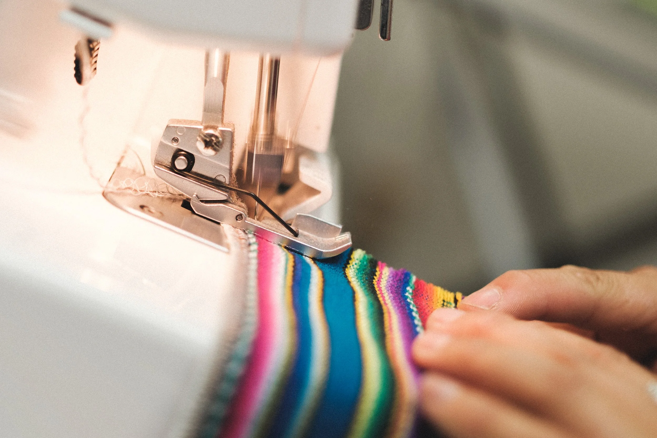 Close-up of a sewing machine sewing a colorful rainbow-striped fabric.