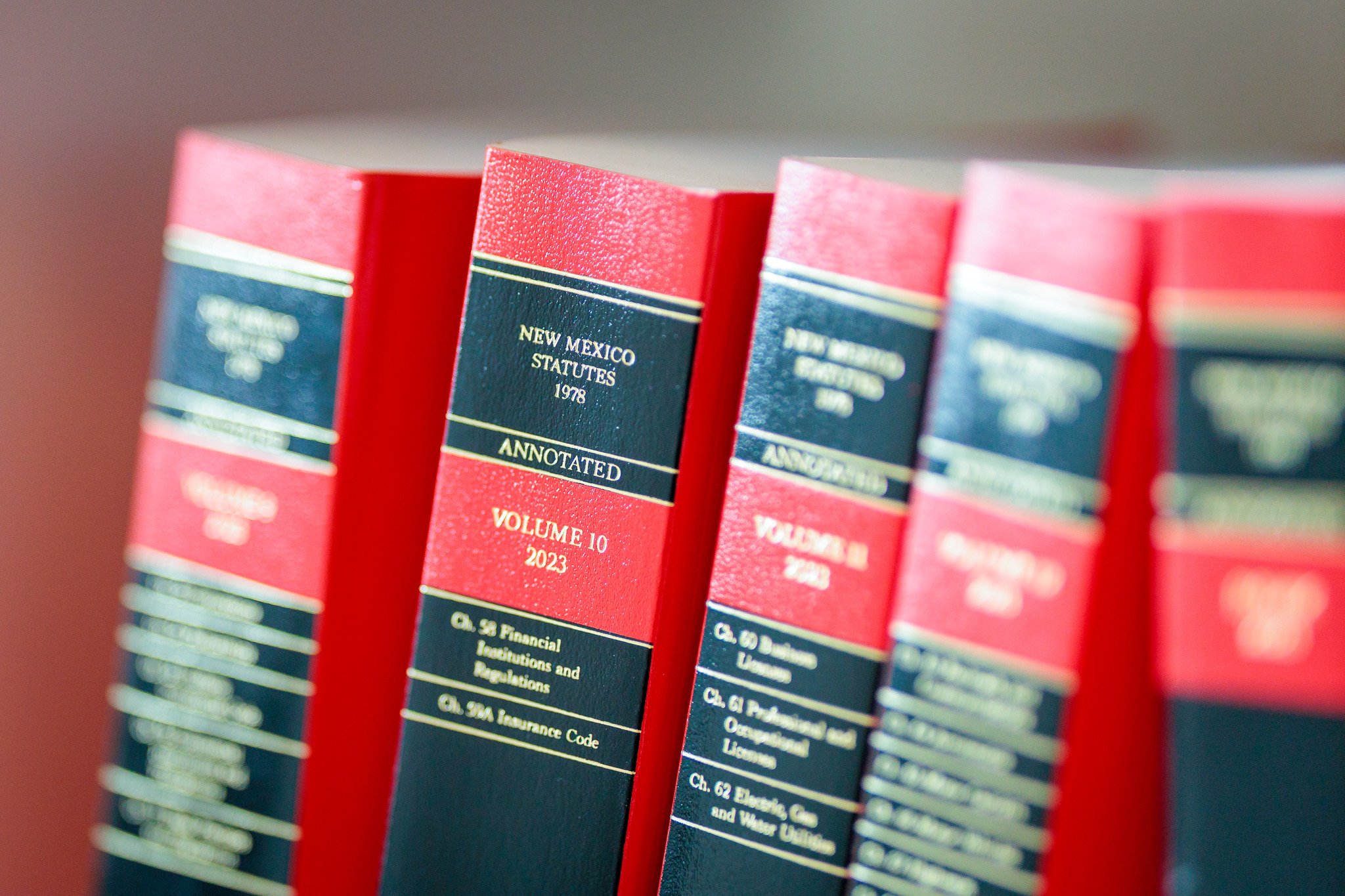 Close-up of New Mexico statutes law books, red and blue spines, titled 'New Mexico Statutes 1978' and 'Volume 10 2023'.
