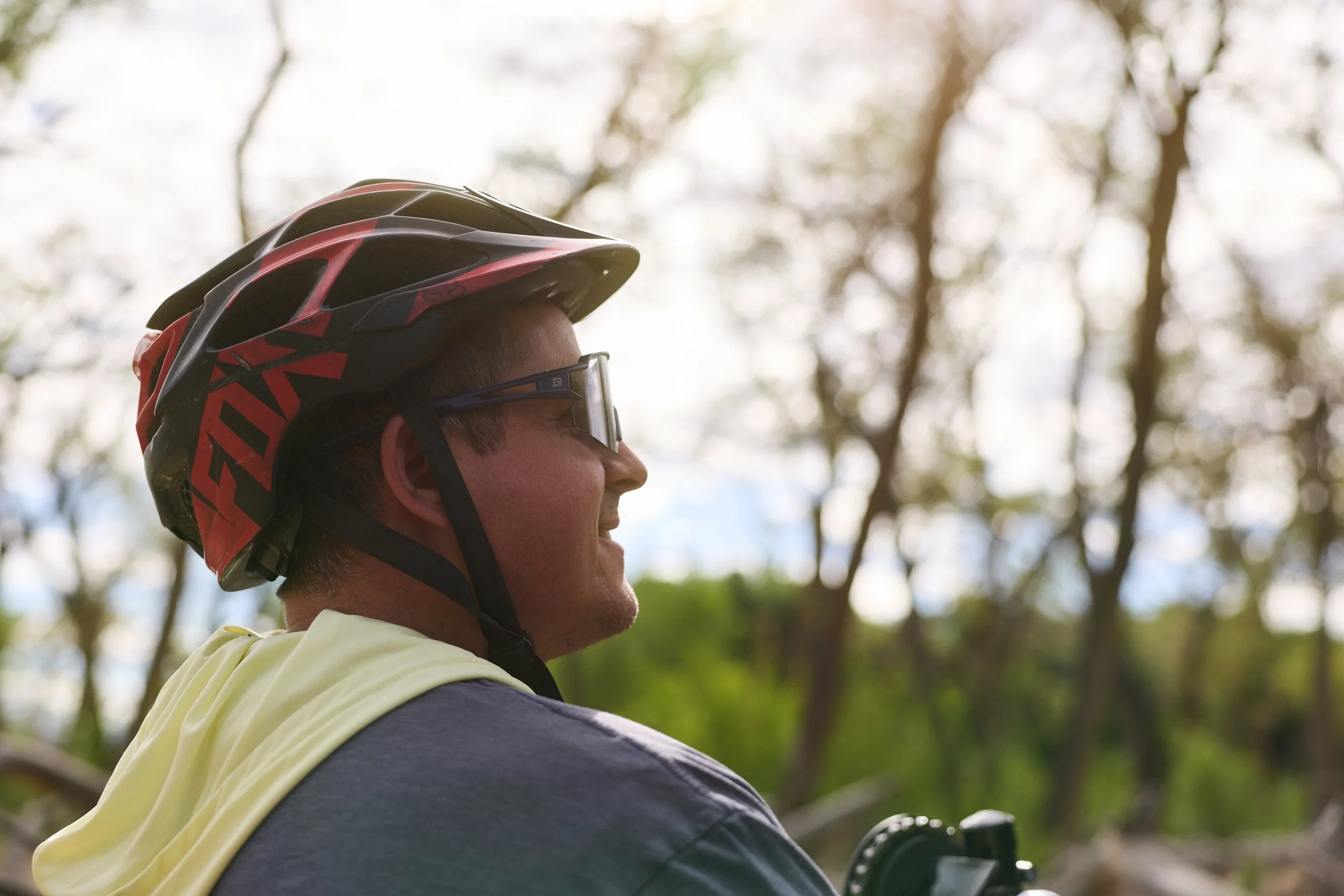 A man wearing a bike helmet and sunglasses, outdoors among trees, during daytime.
