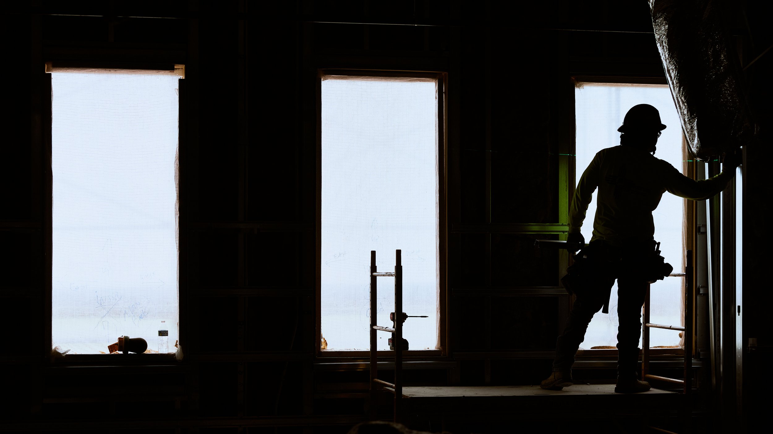 Construction worker in hard hat working inside a building under construction, with large windows in the background.