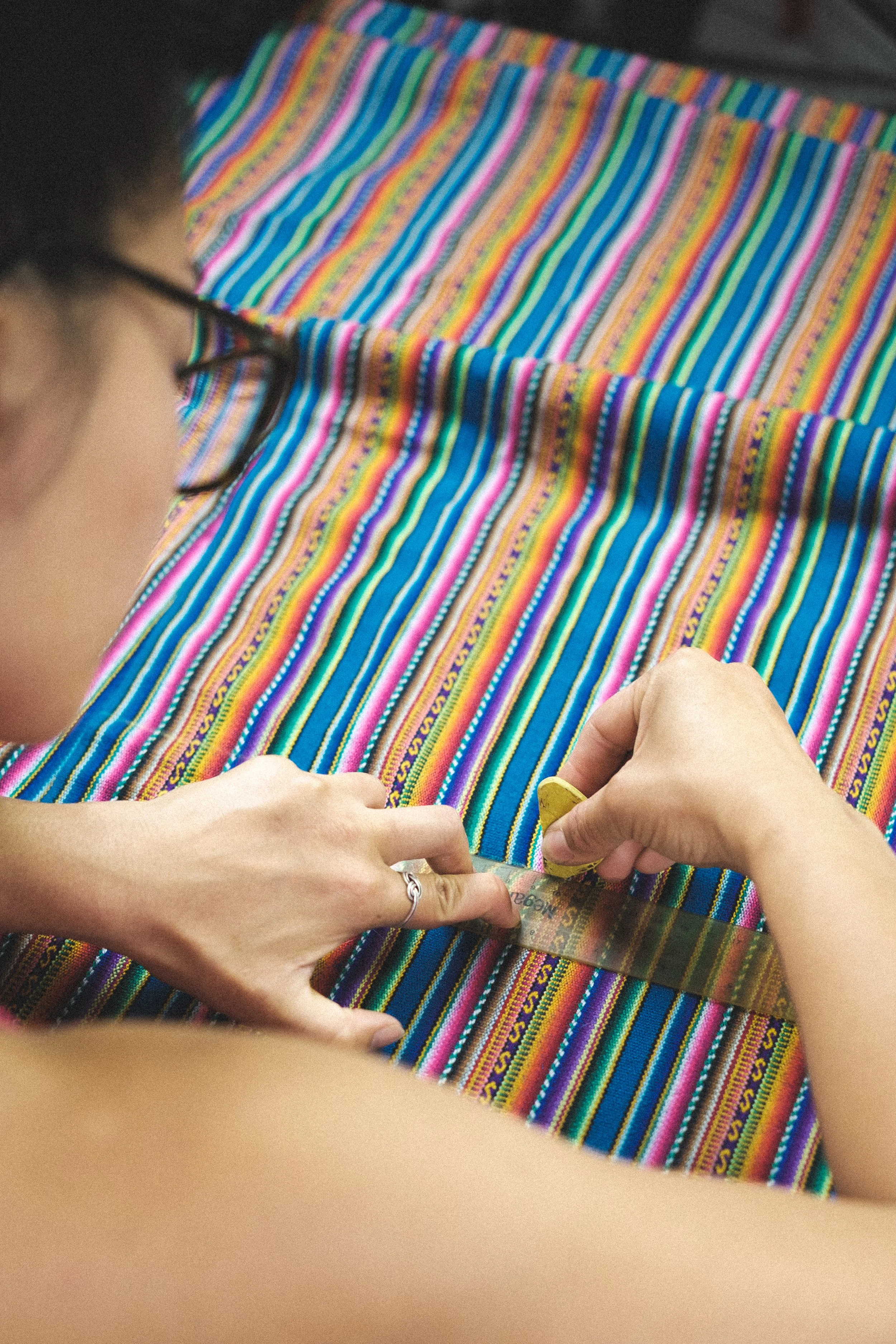 Person sewing a colorful striped textile with a sewing machine.