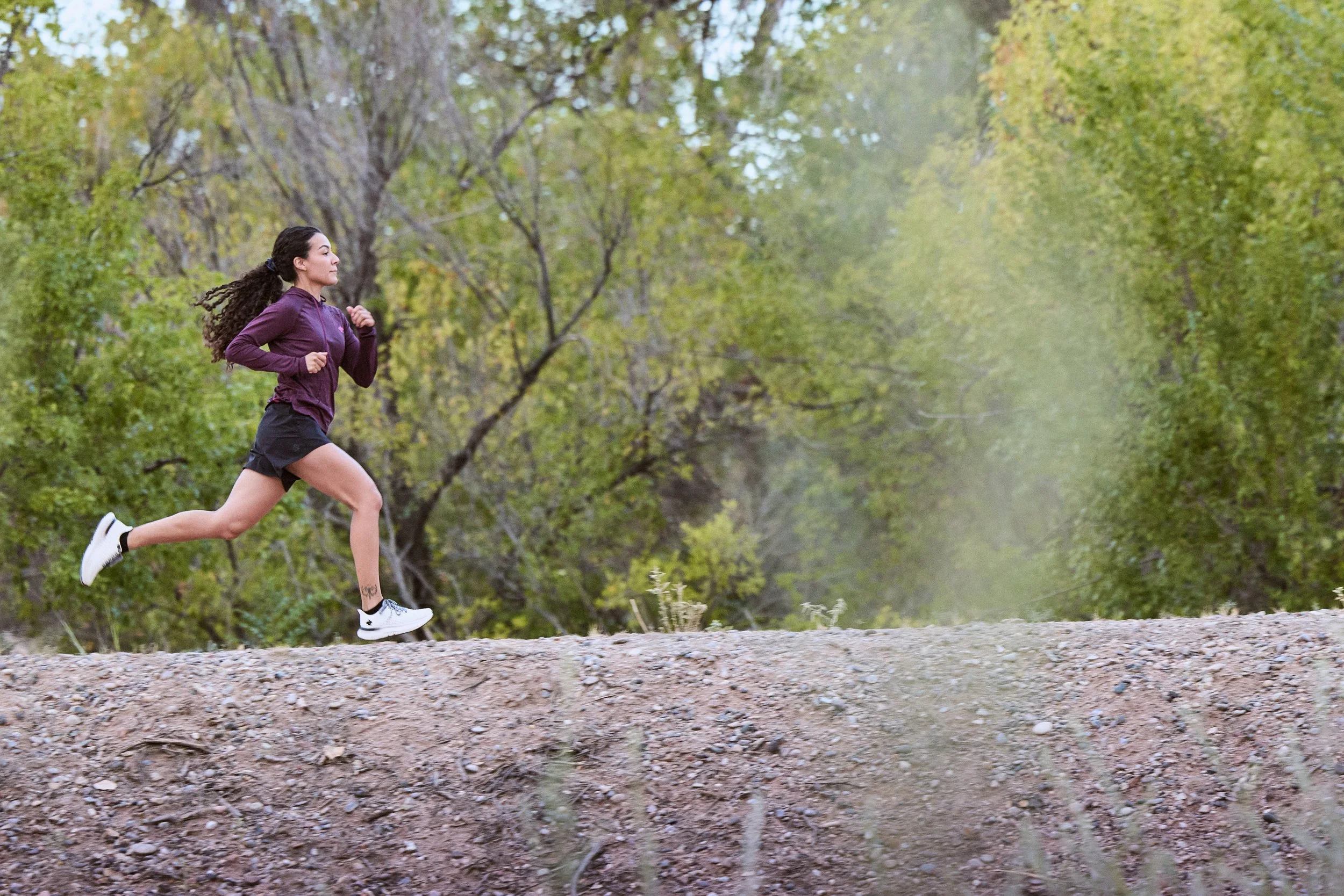 Young woman running on a dirt trail through a lush green forest.