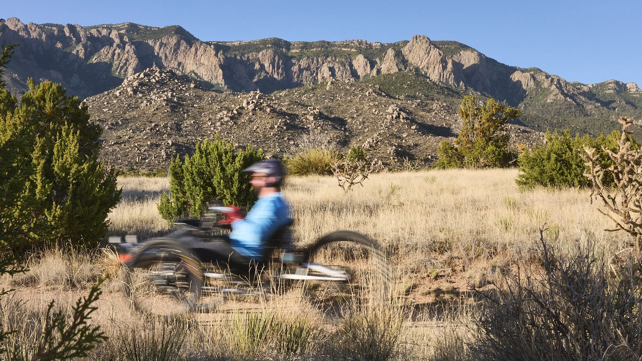 A person riding an all-terrain vehicle (ATV) on a dirt trail in a desert landscape with mountains in the background and sparse vegetation.