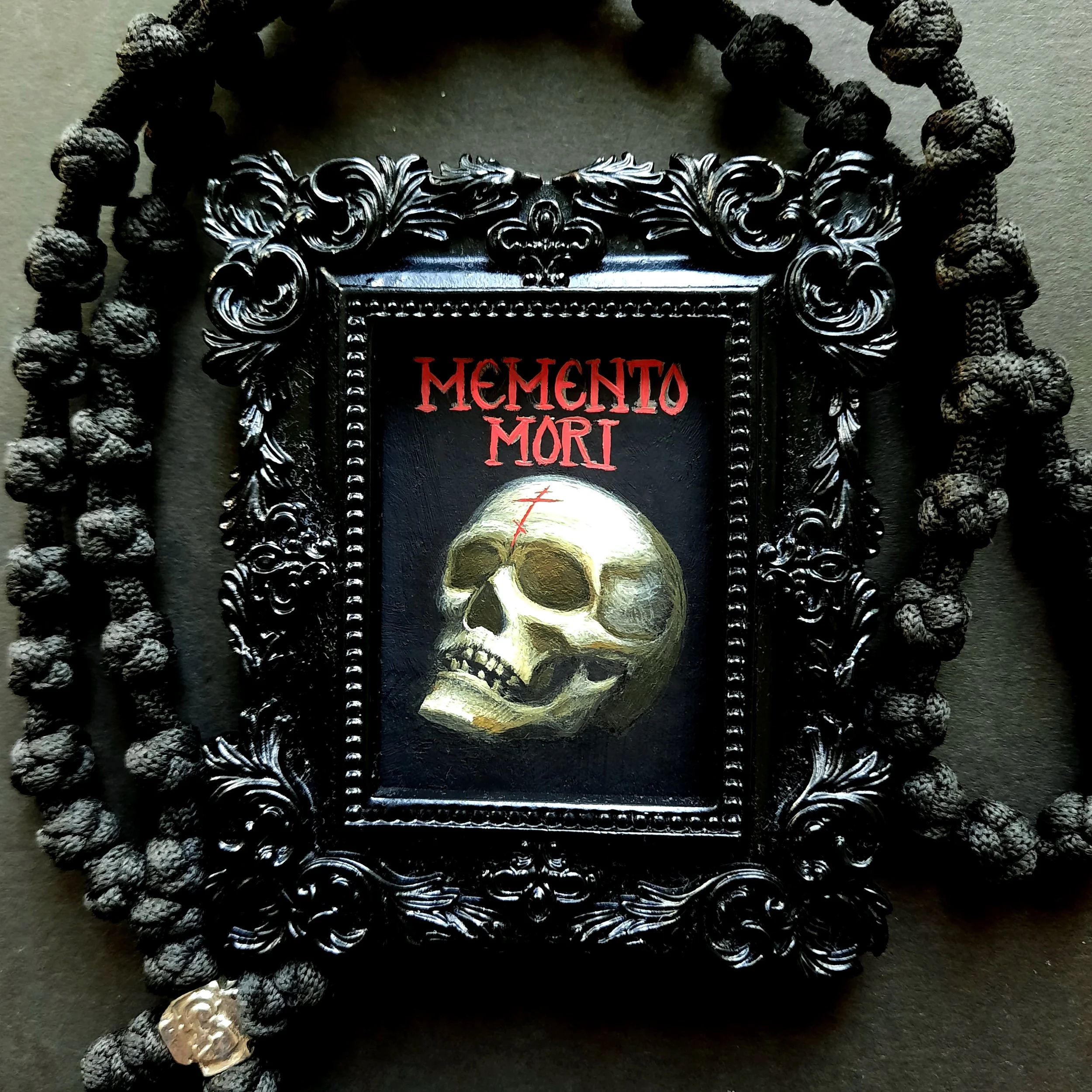 A painting of a skull with the words "Memento Mori" at the top. A black background is behind it and it is surrounded by a floral black frame.