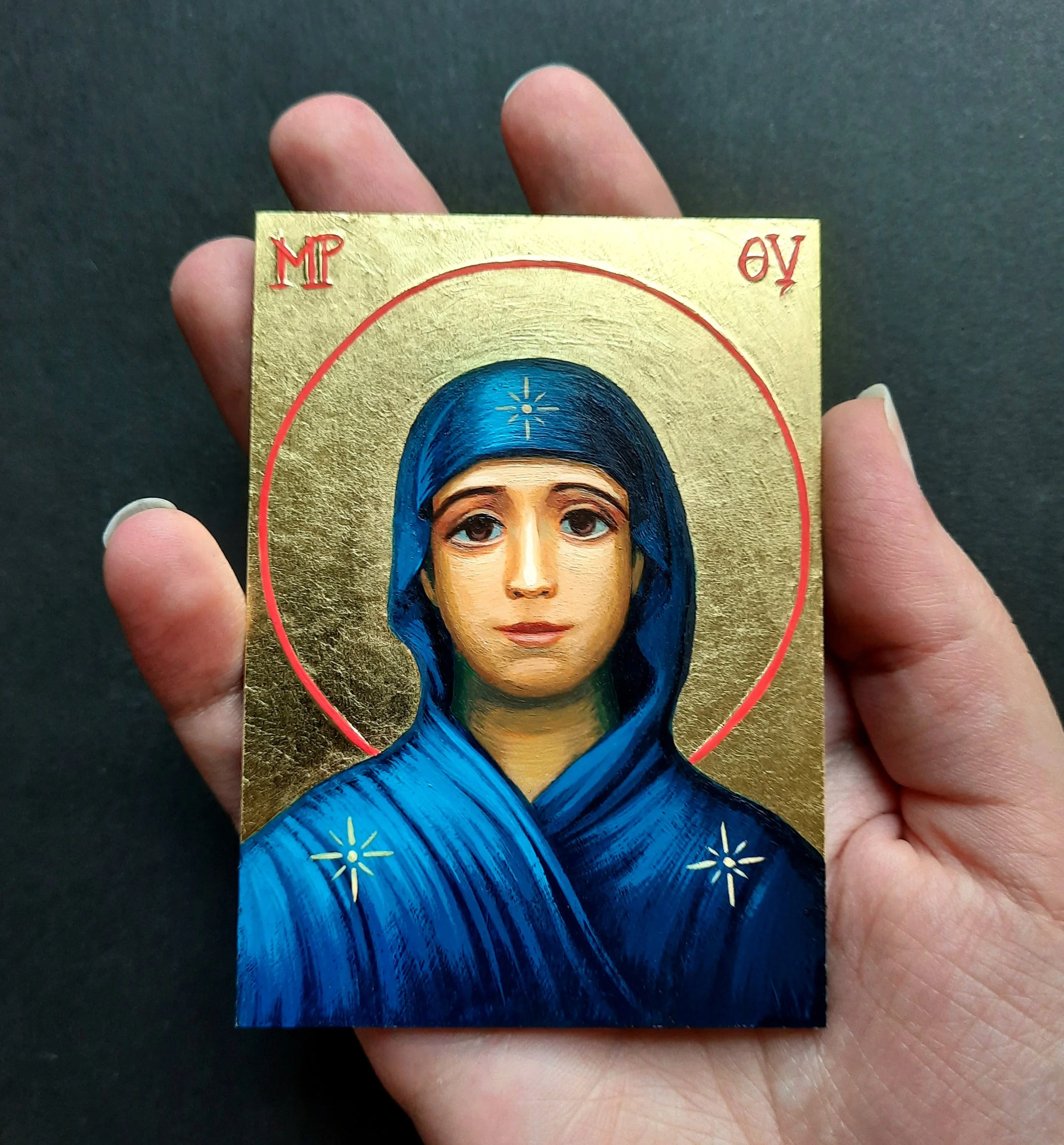 A hand is holding an Orthodox icon depicting the Theotokos with a golden background.
