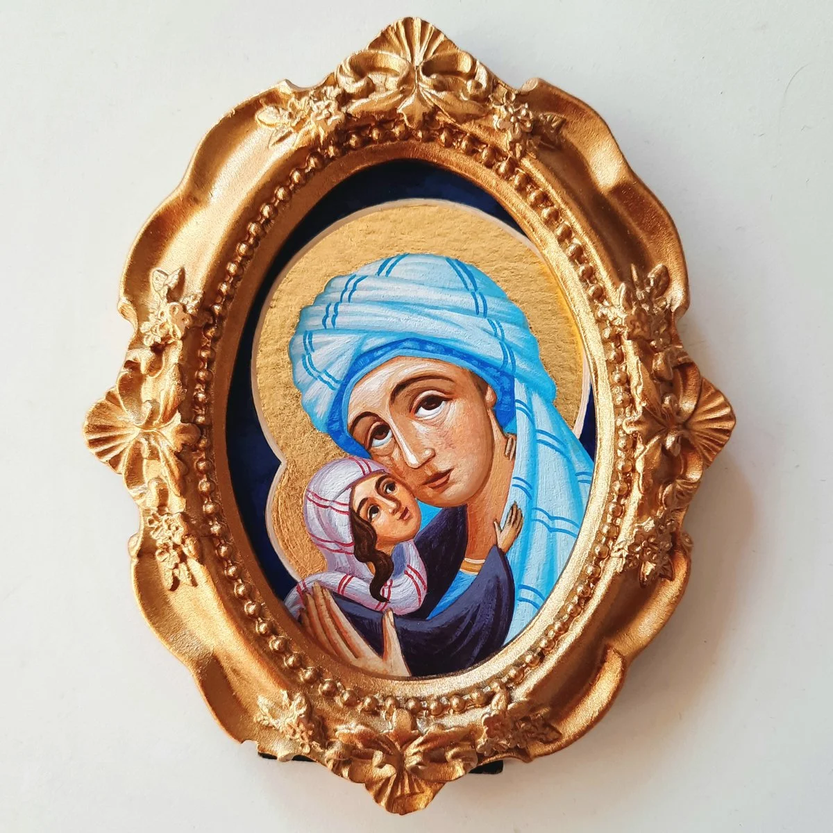 An Orthodox icon depicting St. Anna holding baby Mother Mary, surrounded by a gold ornate frame.