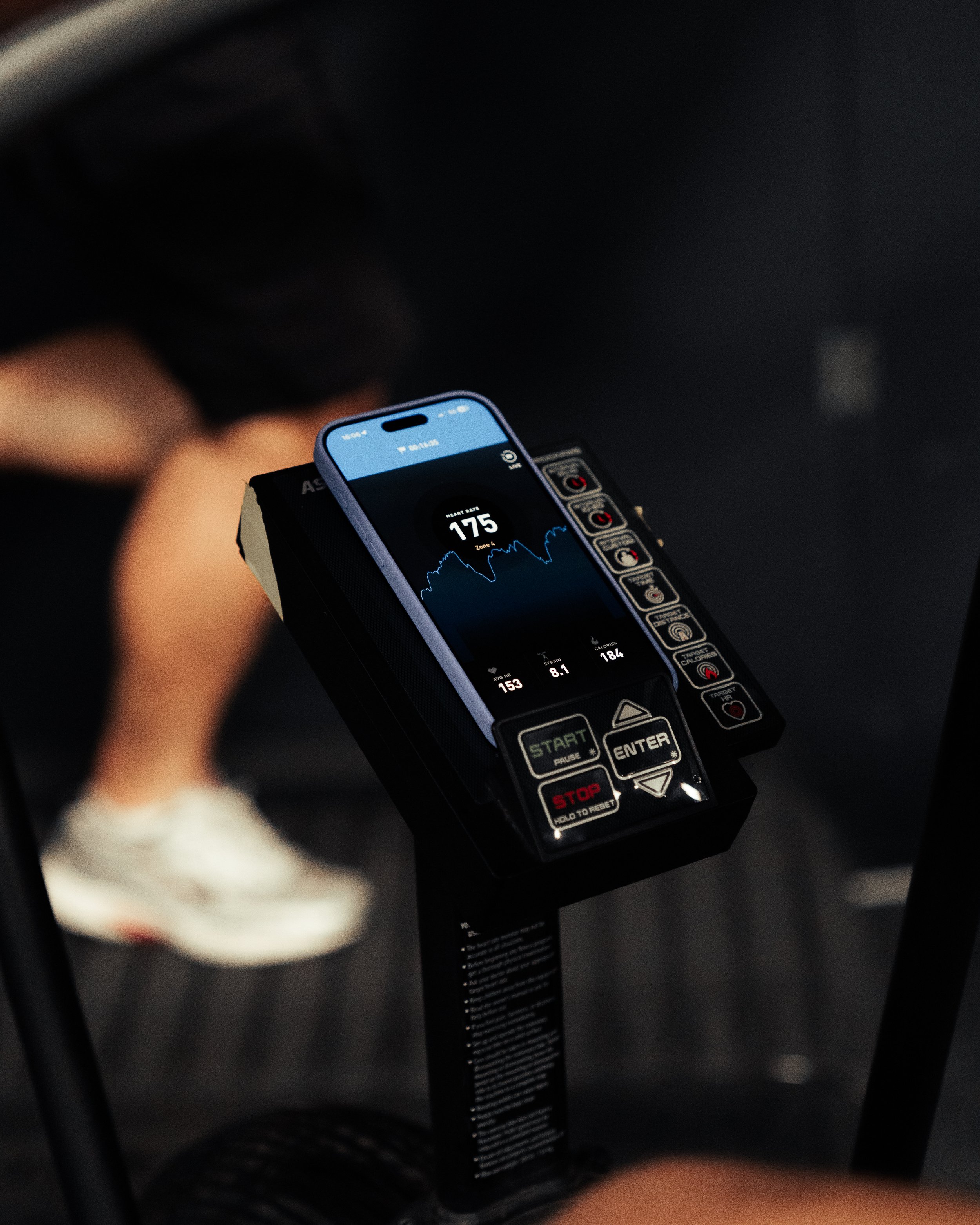 Close-up of a fitness tracker on a smartphone screen showing a heart rate of 175 beats per minute, with an exercise machine in the background.