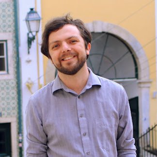 Chris Parthemos wears a grey button down shirt, sports a close-trimmed beard, and smiles warmly at the camera.