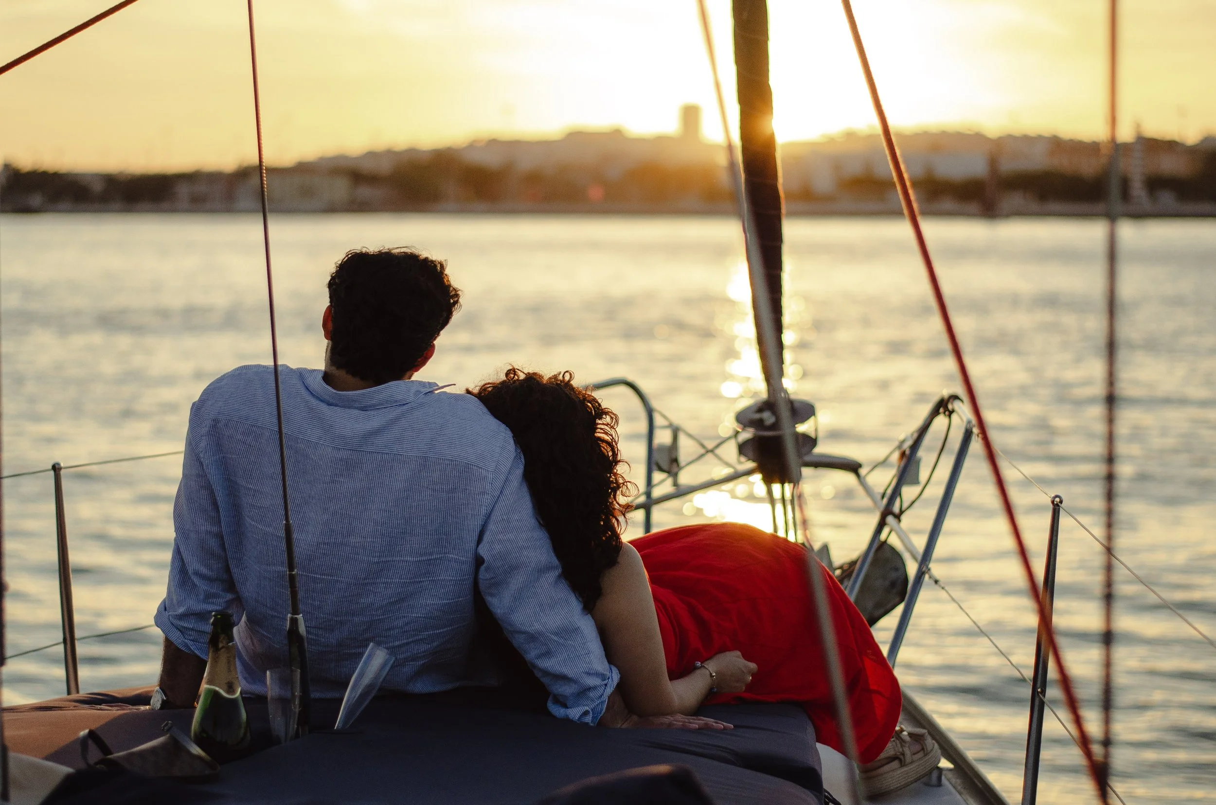 A couple sitting together on a boat at sunset, looking out over the water.