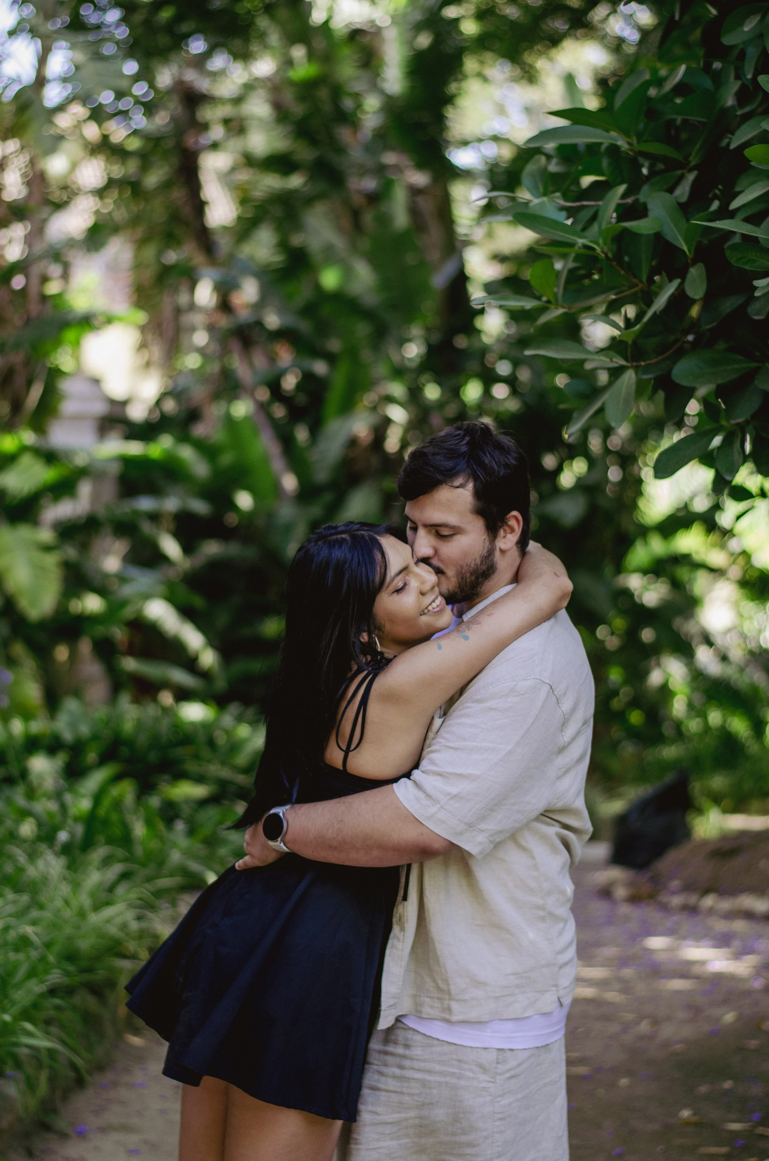 A man and woman embracing in a lush green outdoor setting.