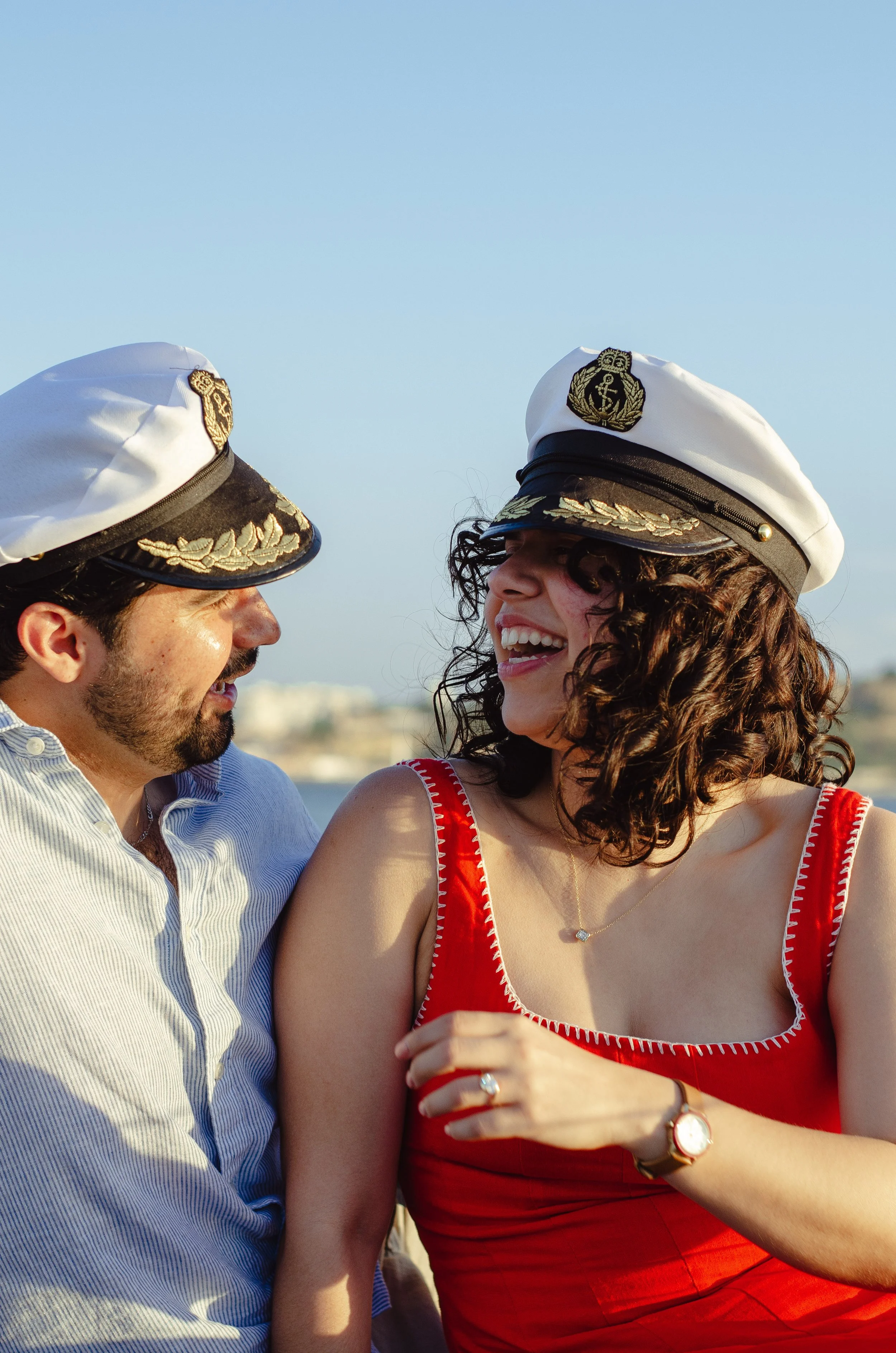 A man and a woman in police captain hats smiling at each other during daytime outdoors.