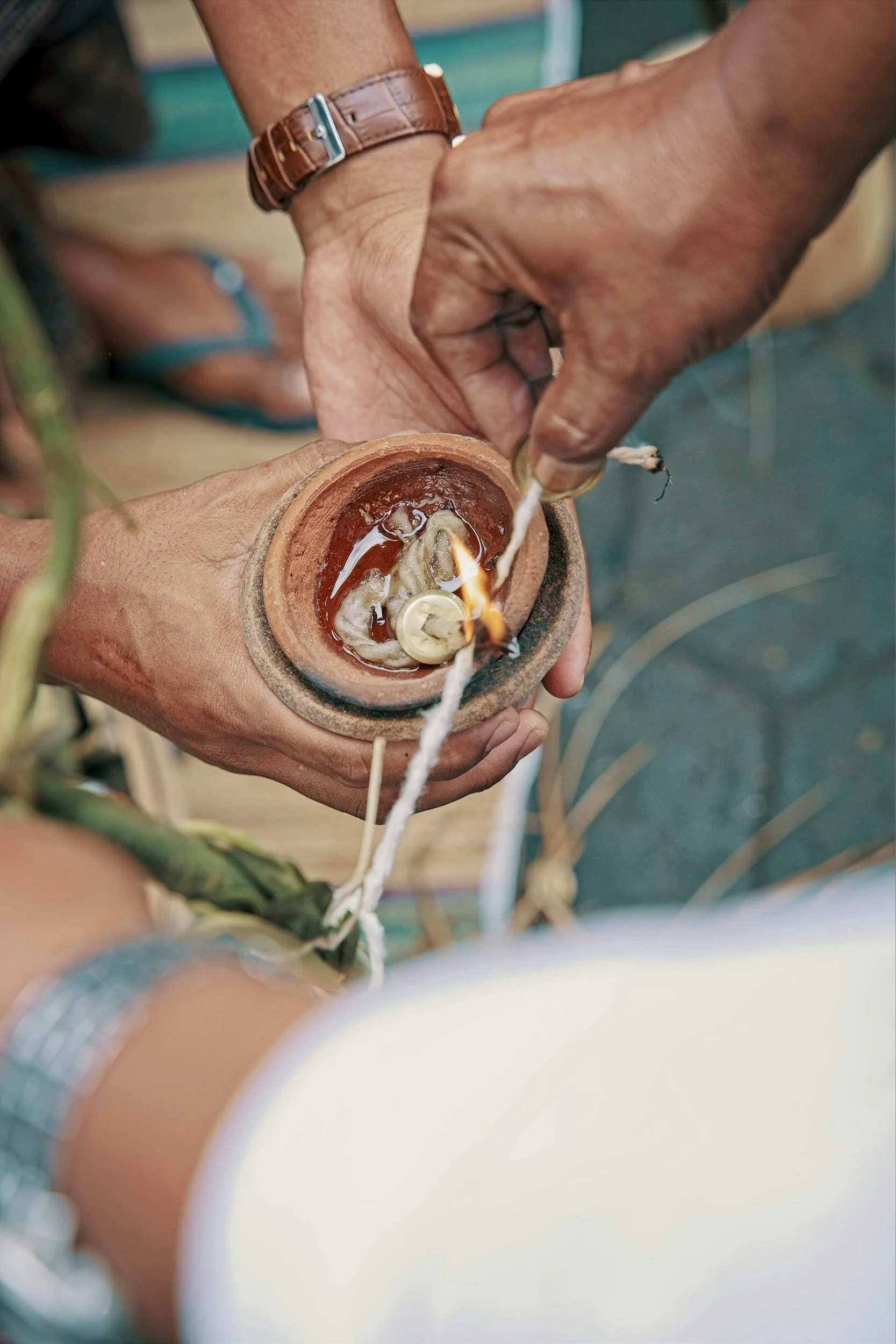Close-up of a person's hand lighting a candle inside an earthen pot with a matchstick.