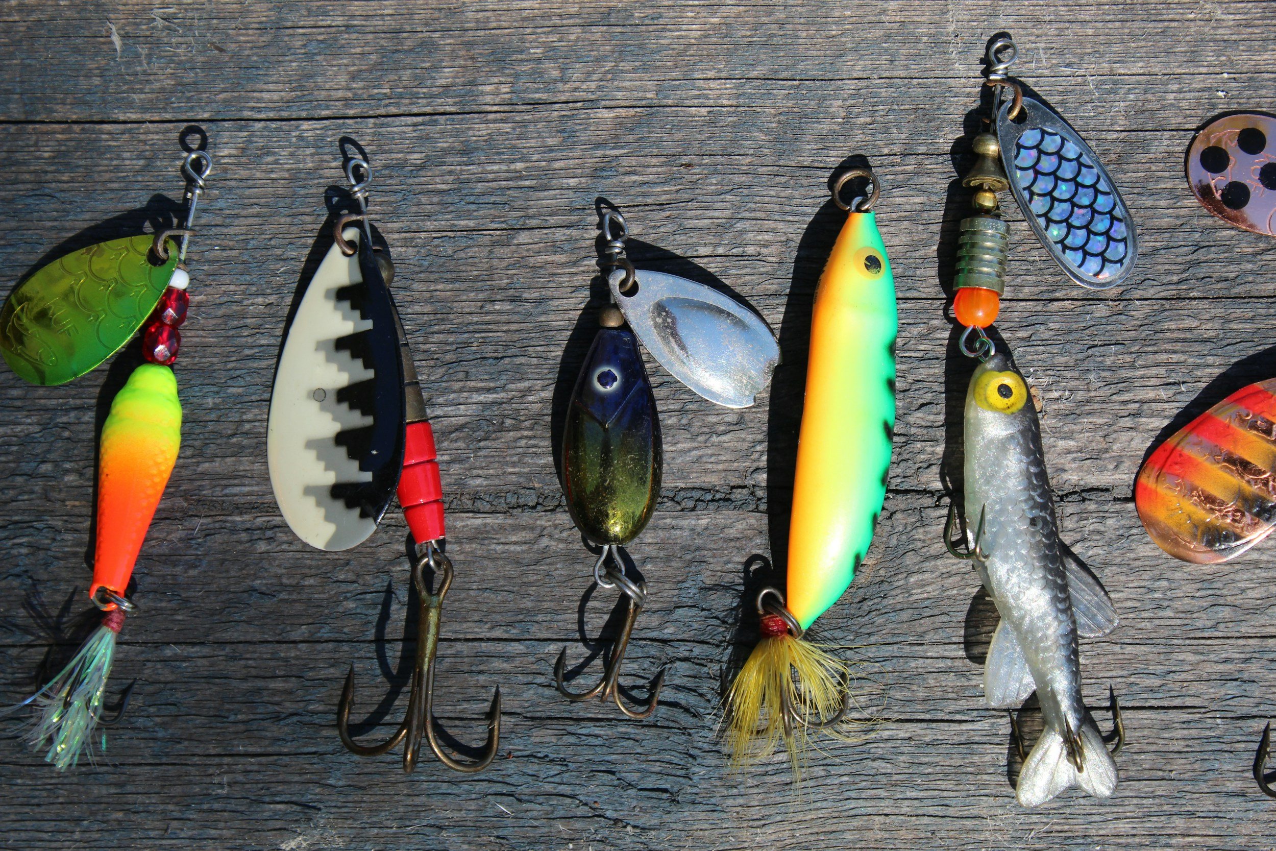 Collection of colorful fishing lures with various designs and shapes laid out on a weathered wooden surface.