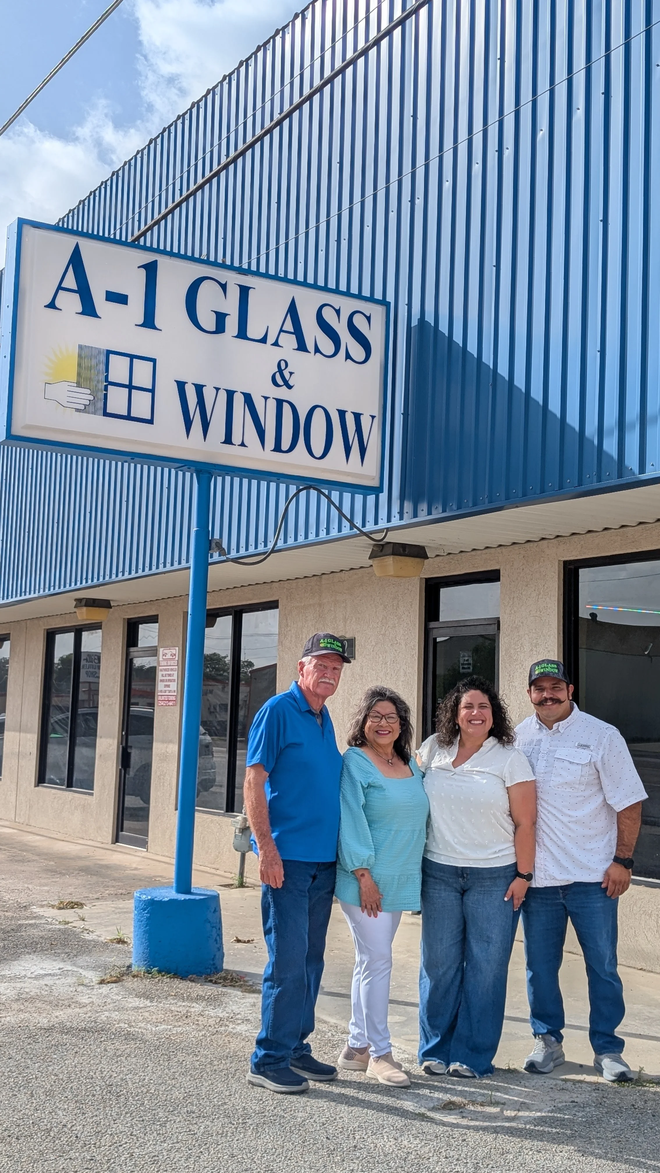 Four people standing outside of a building with a sign that reads 'A-1 Glass & Window.' The group includes two men and two women, all smiling and dressed casually.