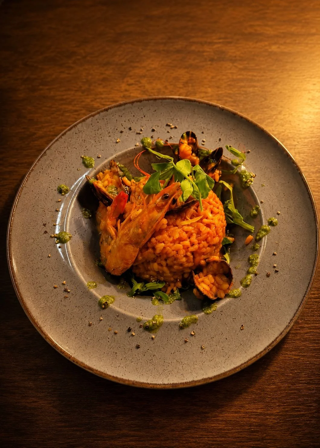 A plate of seafood risotto garnished with greens and herbs, served on a dark wooden table.