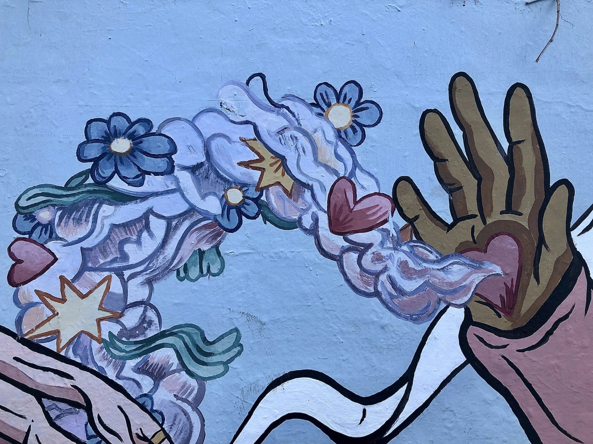 Close-up of a colorful, abstract mural featuring various flowers, hearts, and a brown hand outlined in black.