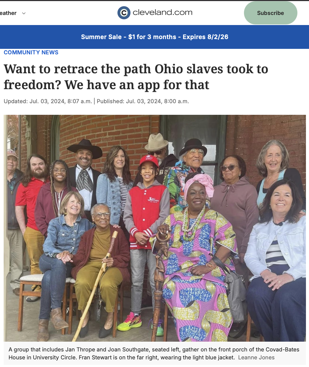 A group of diverse people, including elderly and children, gathered outdoors on a porch in front of a brick house, smiling for a photo.