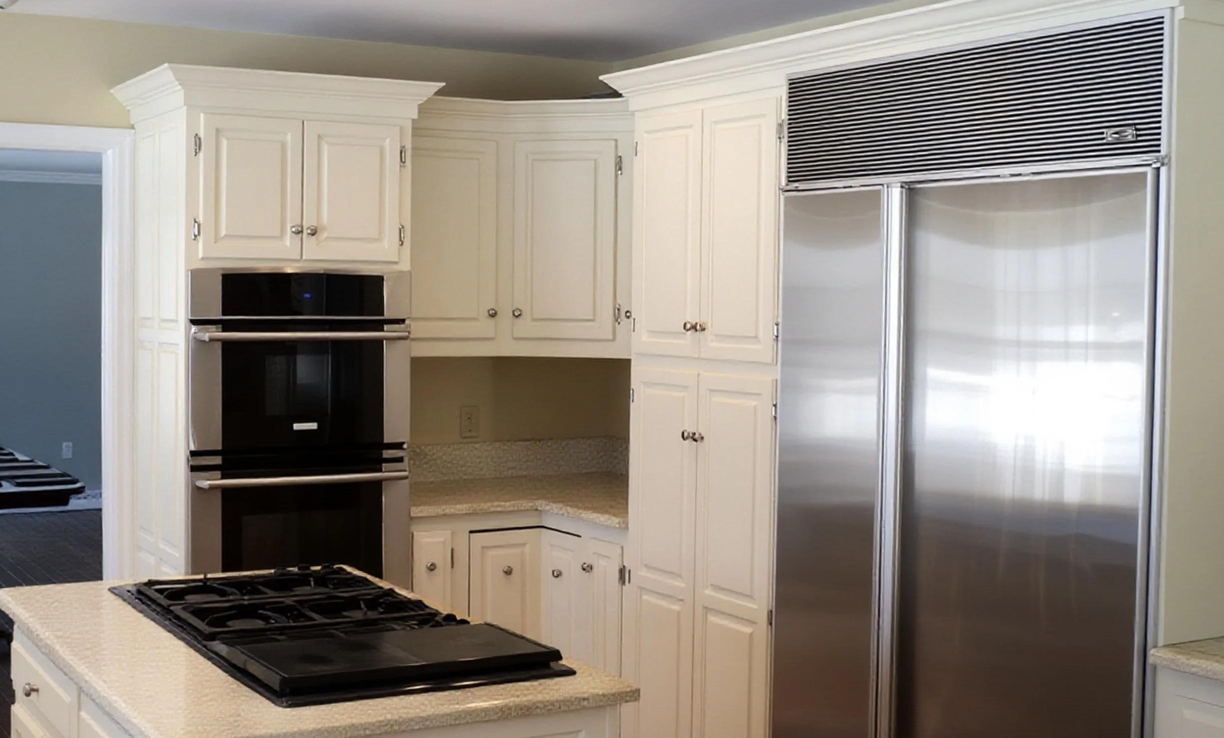 A kitchen with white custom cabinetry, a beige countertop, stainless steel appliances, and a gas stove on a kitchen island.