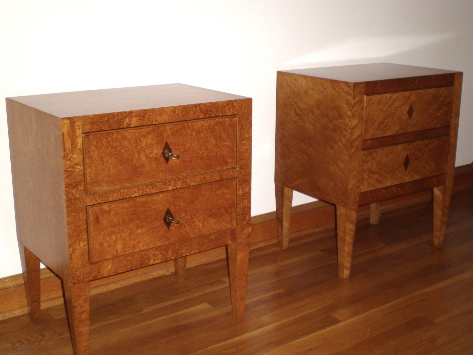 Two custom designed vintage-style wooden dressers with a polished wood finish, standing on wooden legs, positioned against a white wall on a hardwood floor.