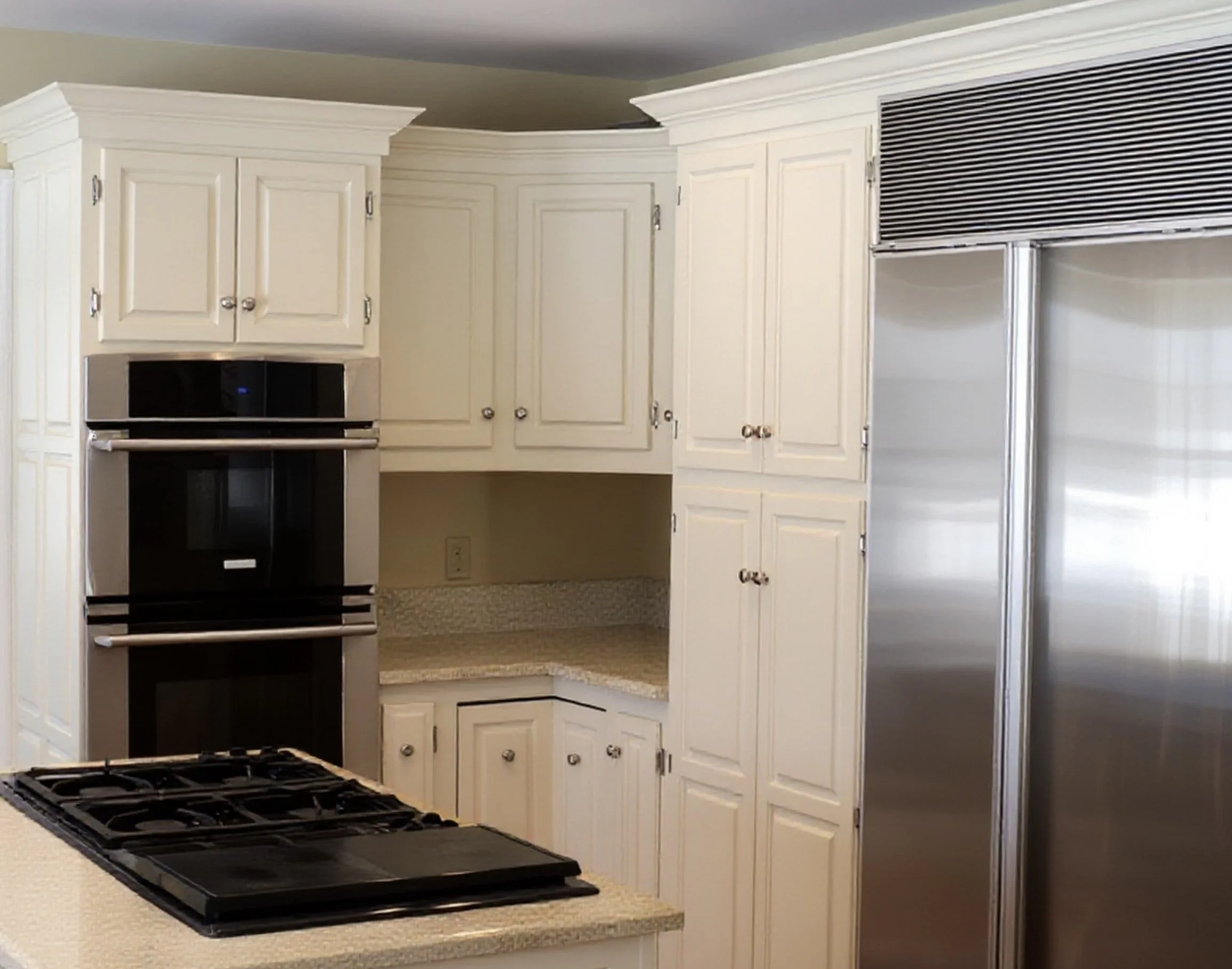 Kitchen with white custom cabinetry, a black stainless steel oven, stove top on a beige granite countertop, and stainless steel refrigerator.
