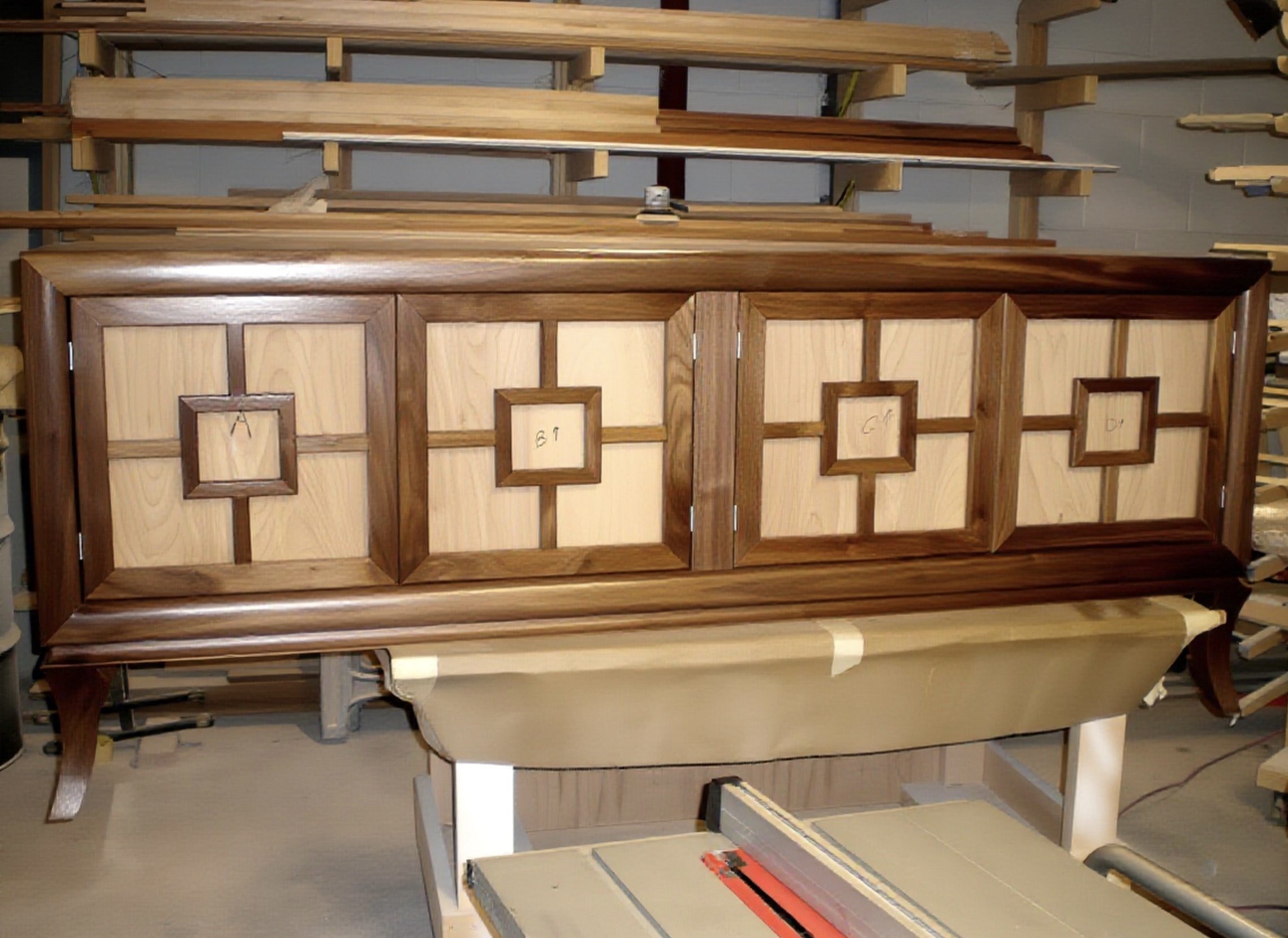 Custom handmade wooden furniture in progress, including large wooden panels and frames, in a workshop setting.