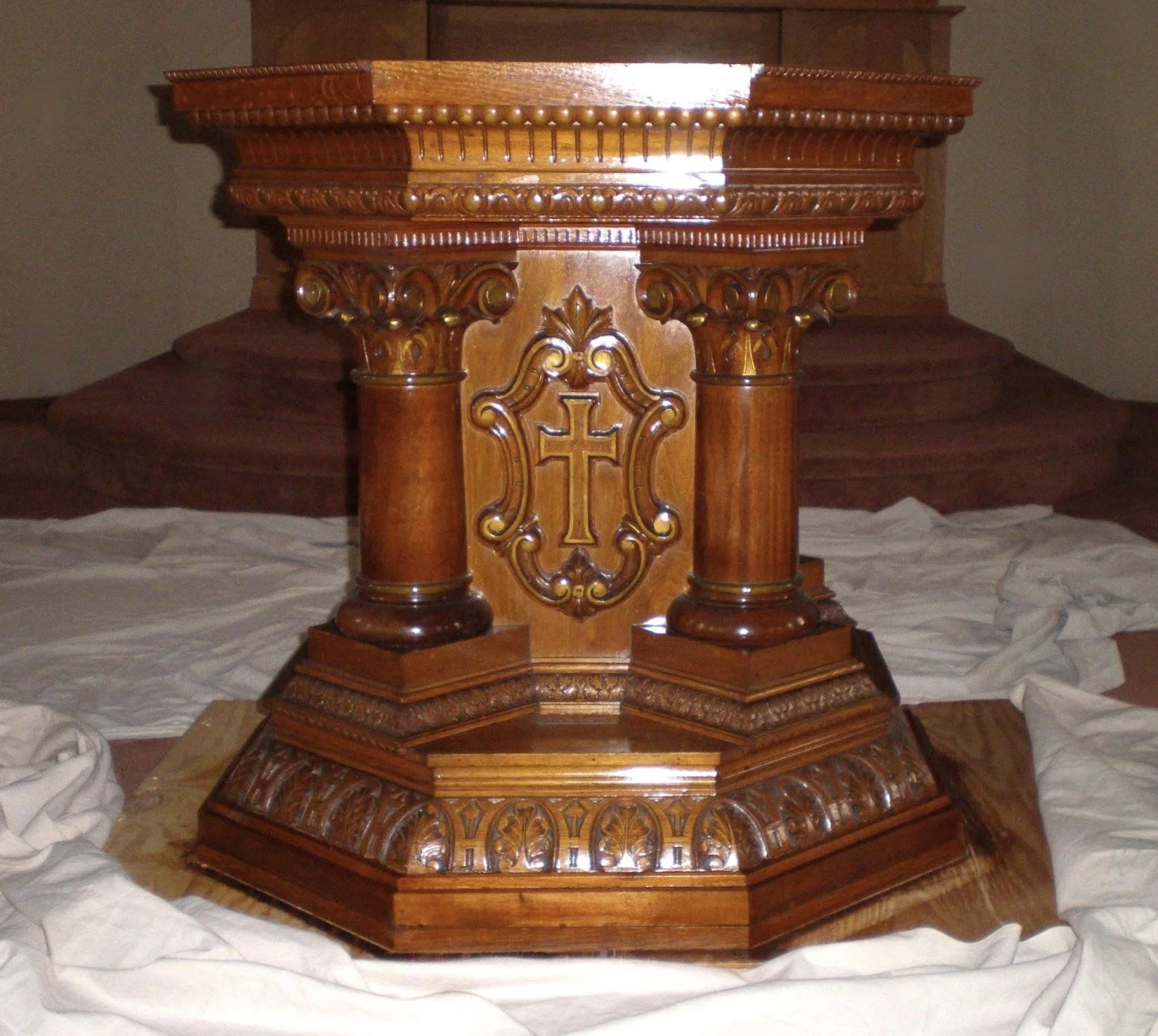 A custom wooden church altar with intricate carvings and a cross emblem in the center, placed on a decorated base.