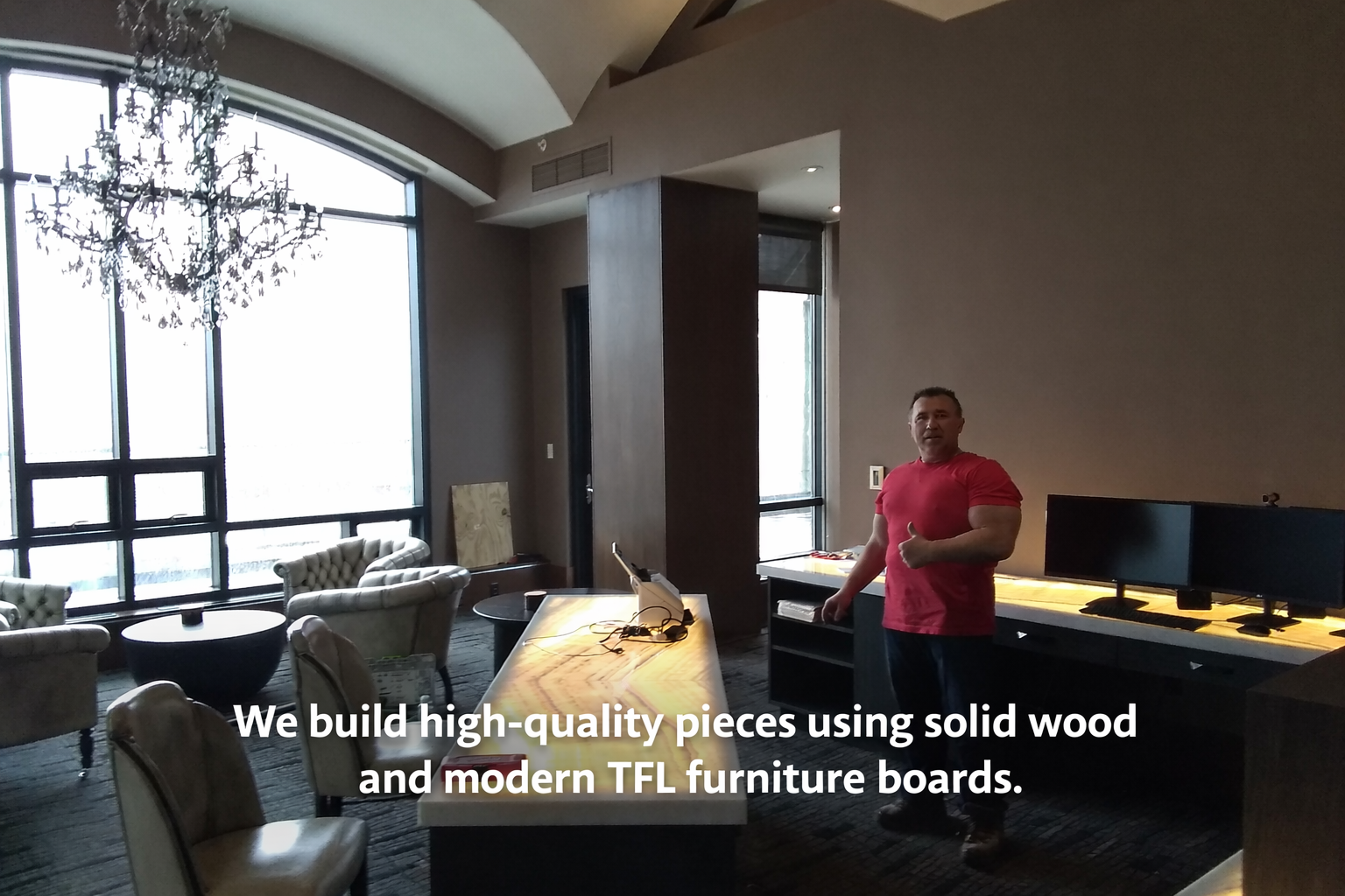 Big John standing in modern lounge with large windows, chandelier, chairs, and custom made desks with dual monitors.