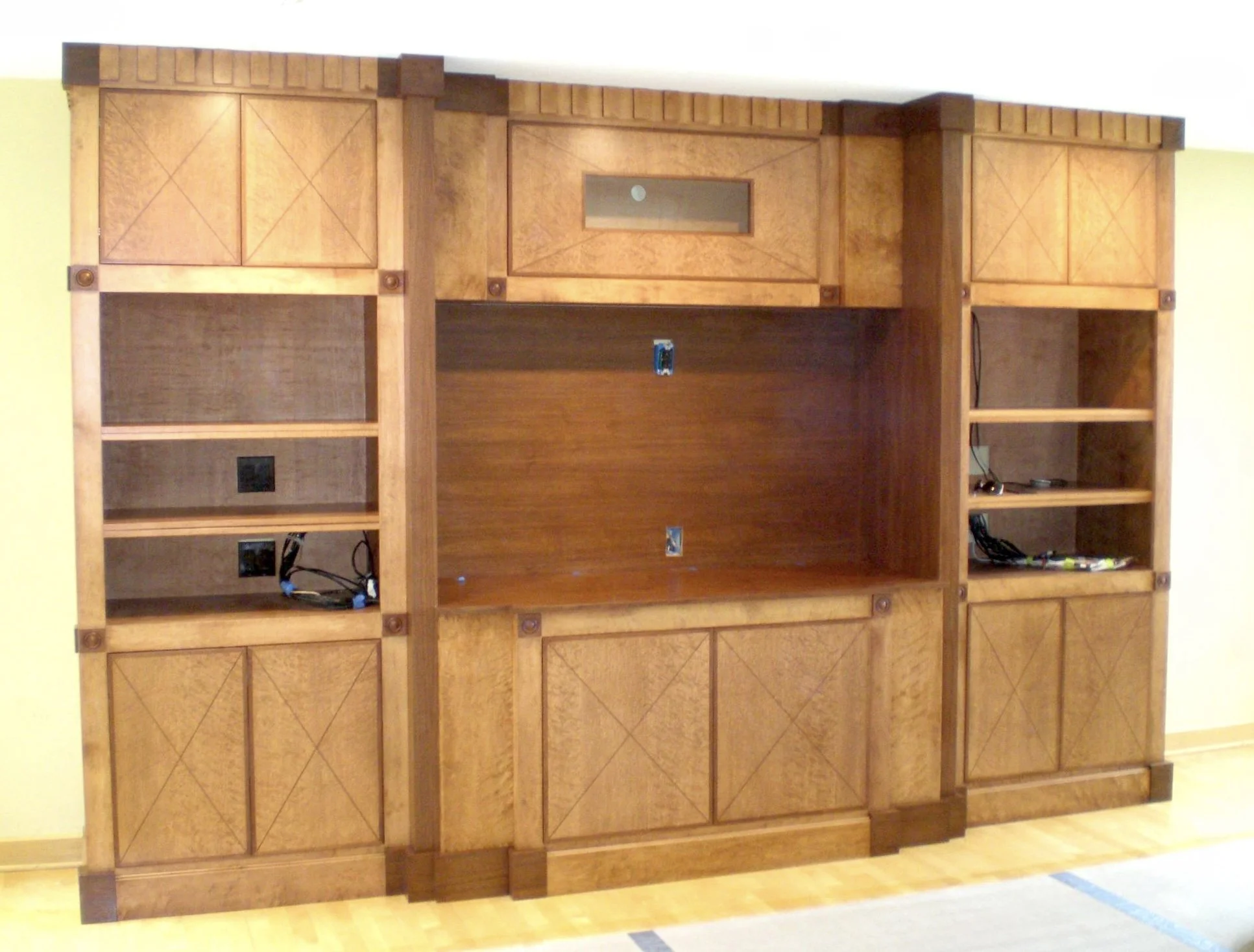 A large custom-ordered wooden entertainment center with multiple shelves and cabinets. The wood has a warm finish, with some portions featuring a darker tone.