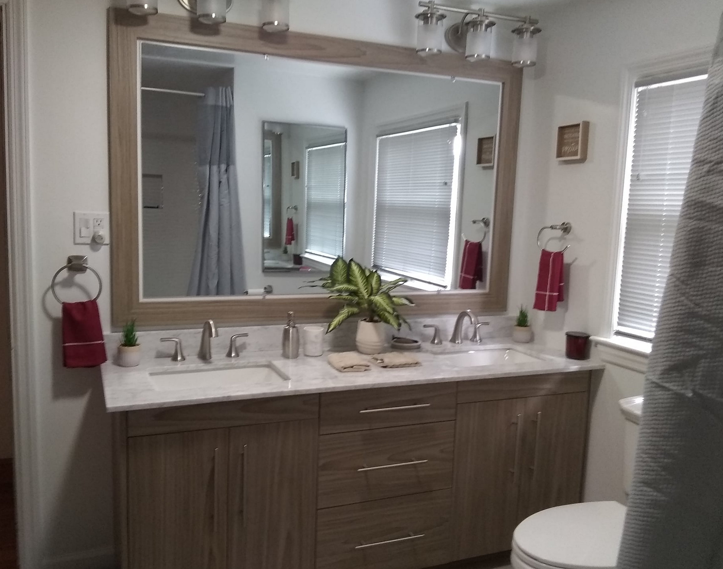 A custom made bathroom vanity with a marble top and a large mirror framed in wood. The bathroom has modern decor.