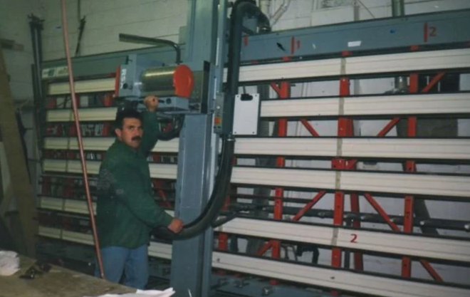 An older picture of a man standing beside an industrial panel saw in a cabinetry shop.