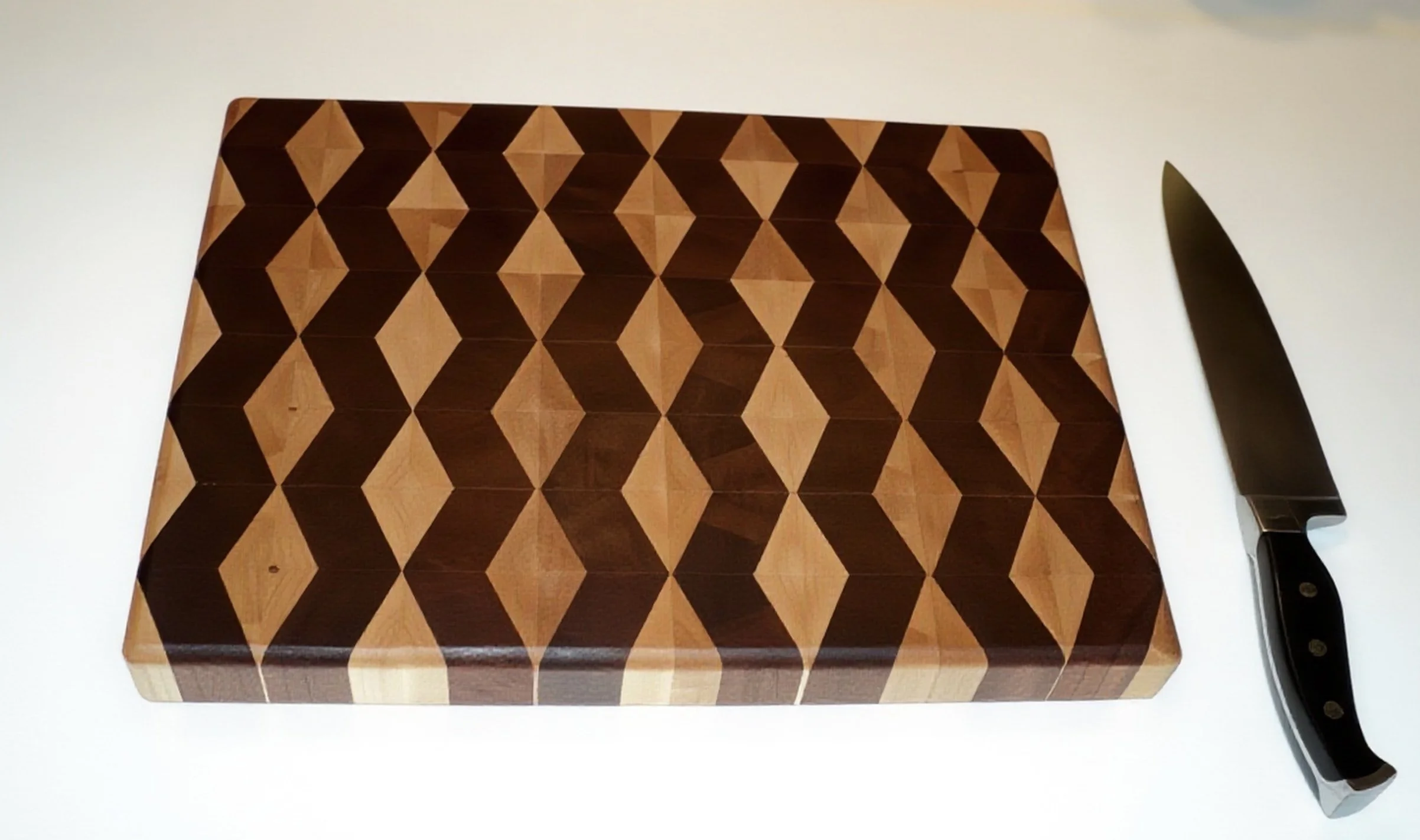 A custom made rectangular wooden cutting board with a geometric pattern of darker and lighter wood triangles forming diamonds. 