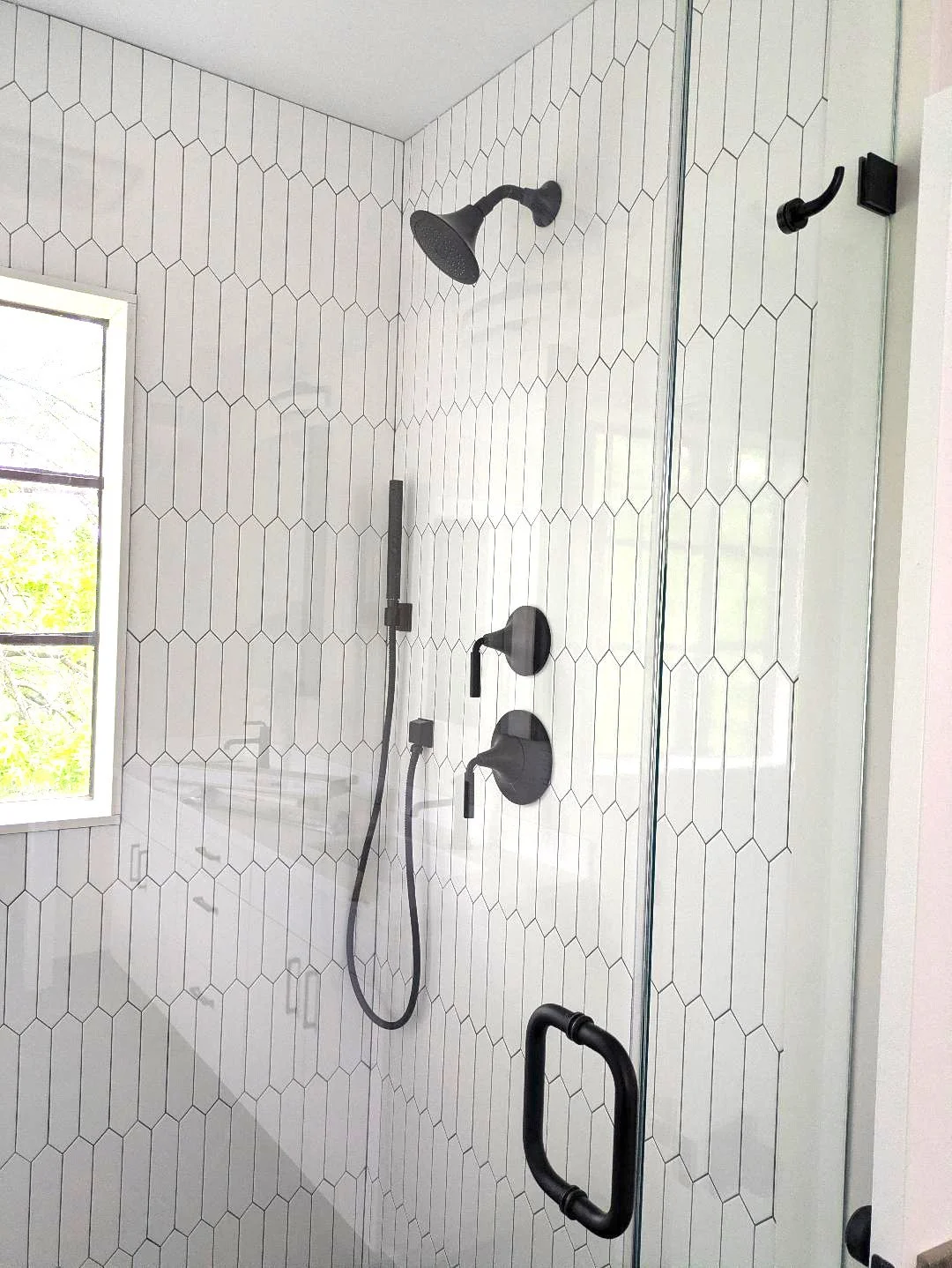 Modern shower with black fixtures, a window, and white hexagonal tiles.