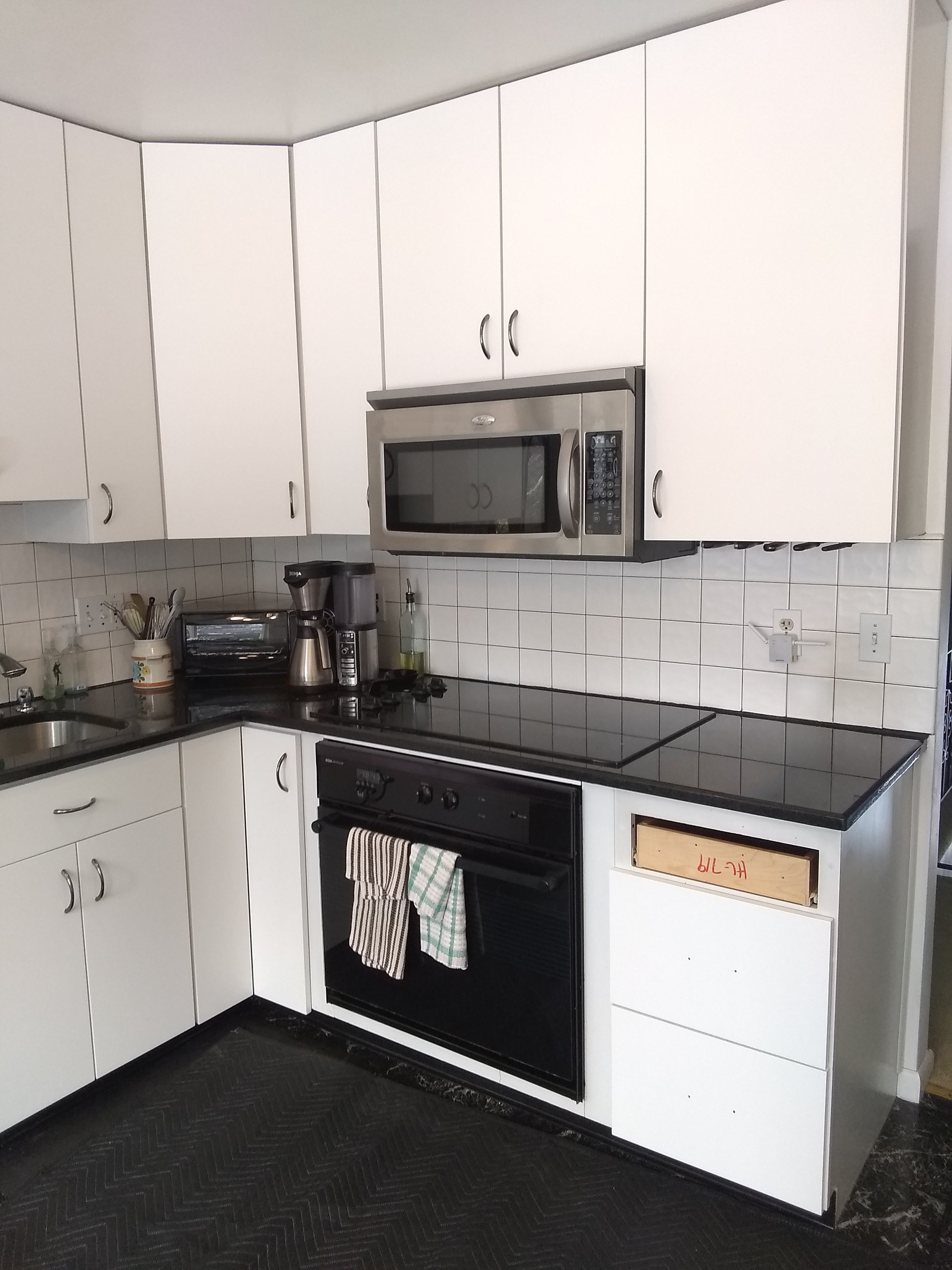 Kitchen with white made-to-order cabinetry, black stove, microwave, coffee maker, and various utensils on the counter.