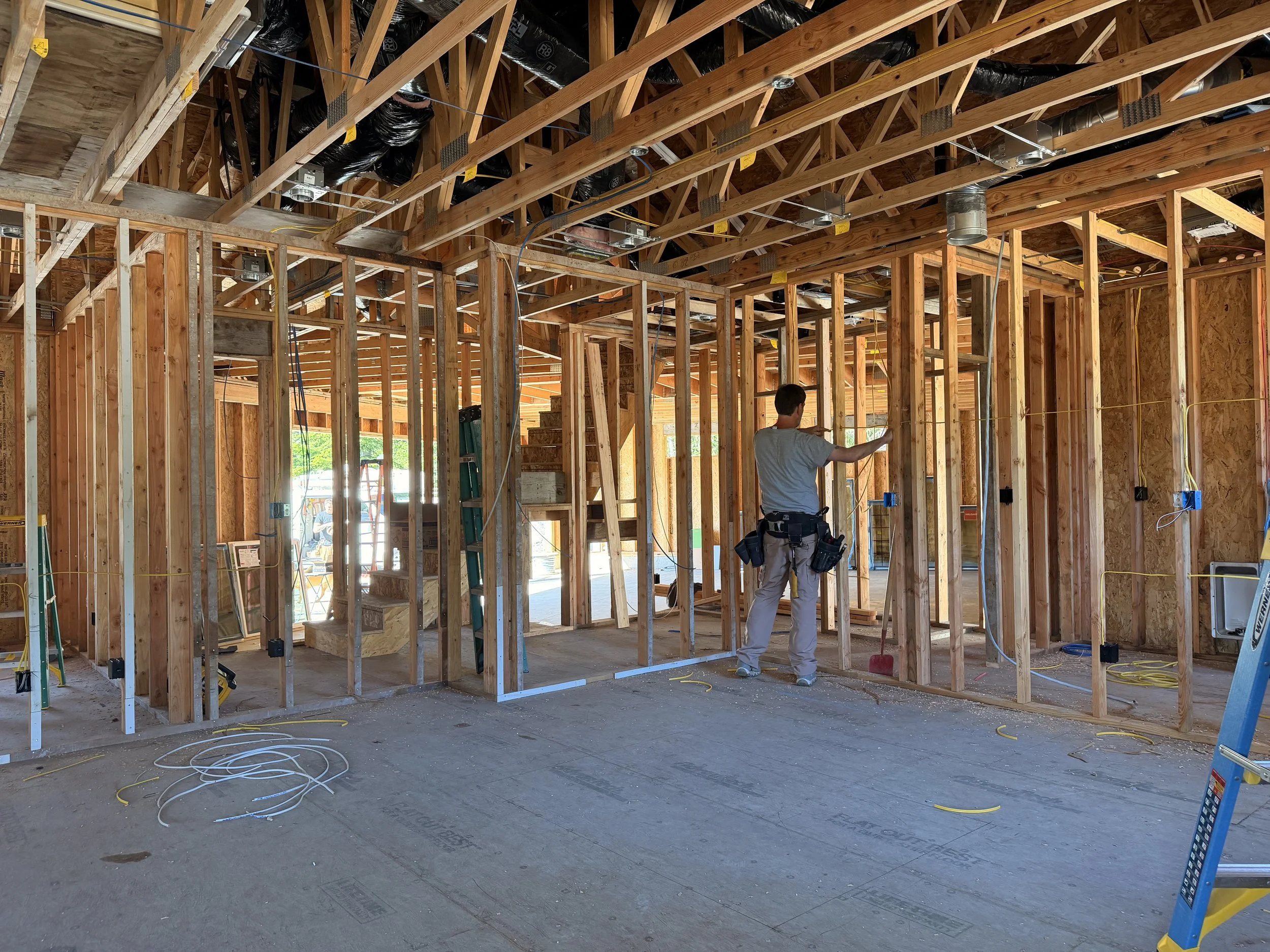 Electrician measuring wall locations for electrical box installation in new construction.