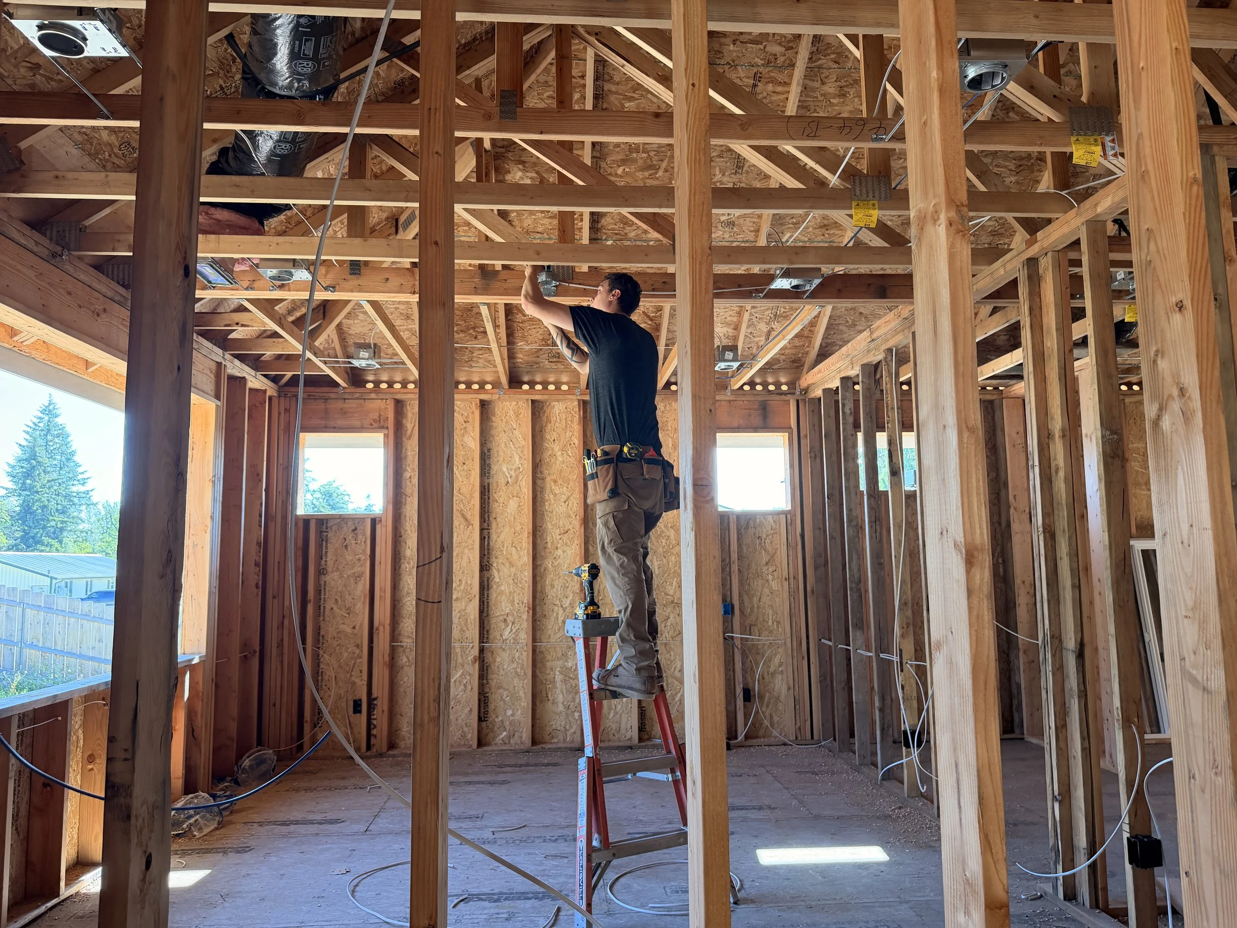 Electrician measuring wall locations for electrical box installation in new construction.