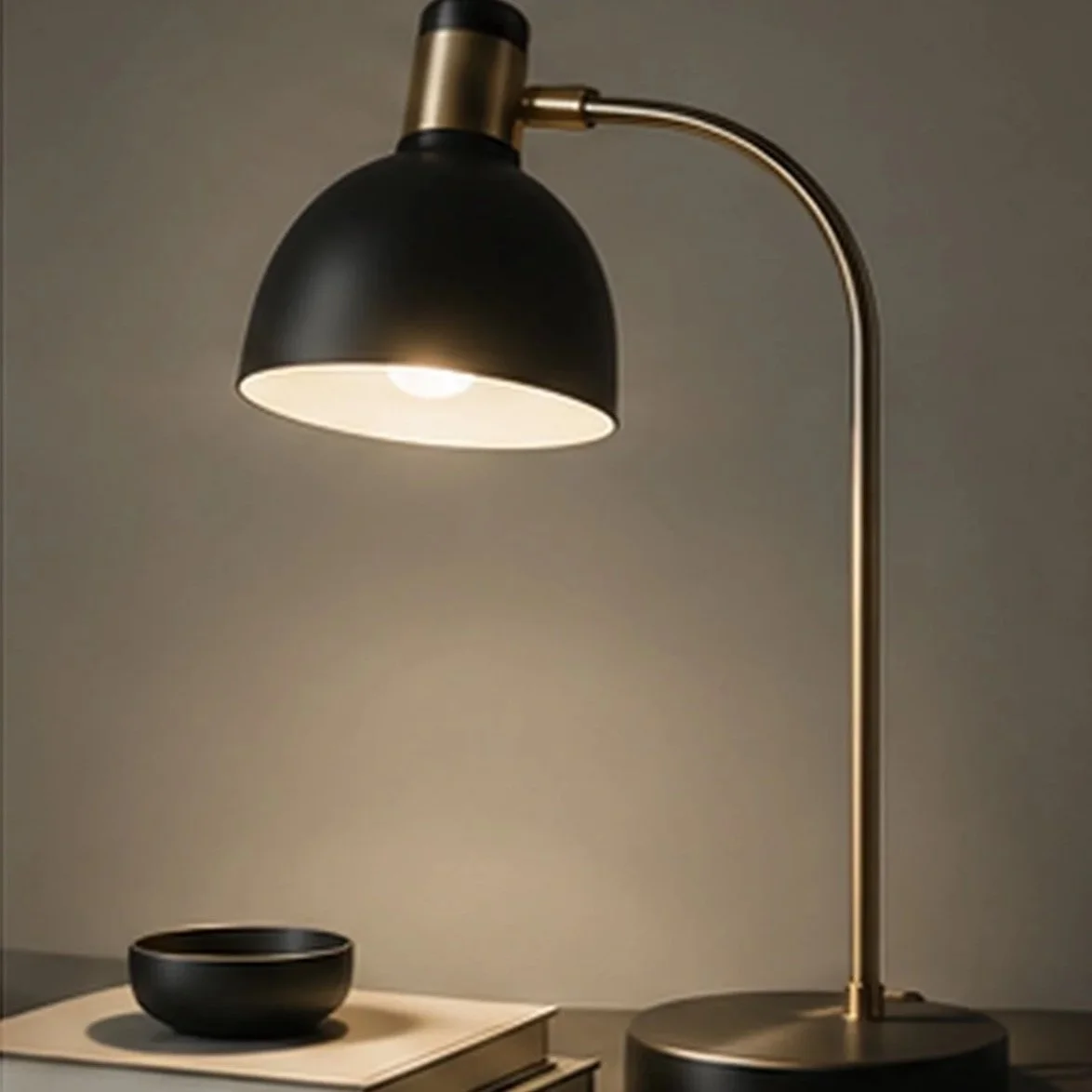 A black and gold desk lamp illuminating a black bowl on a white surface.