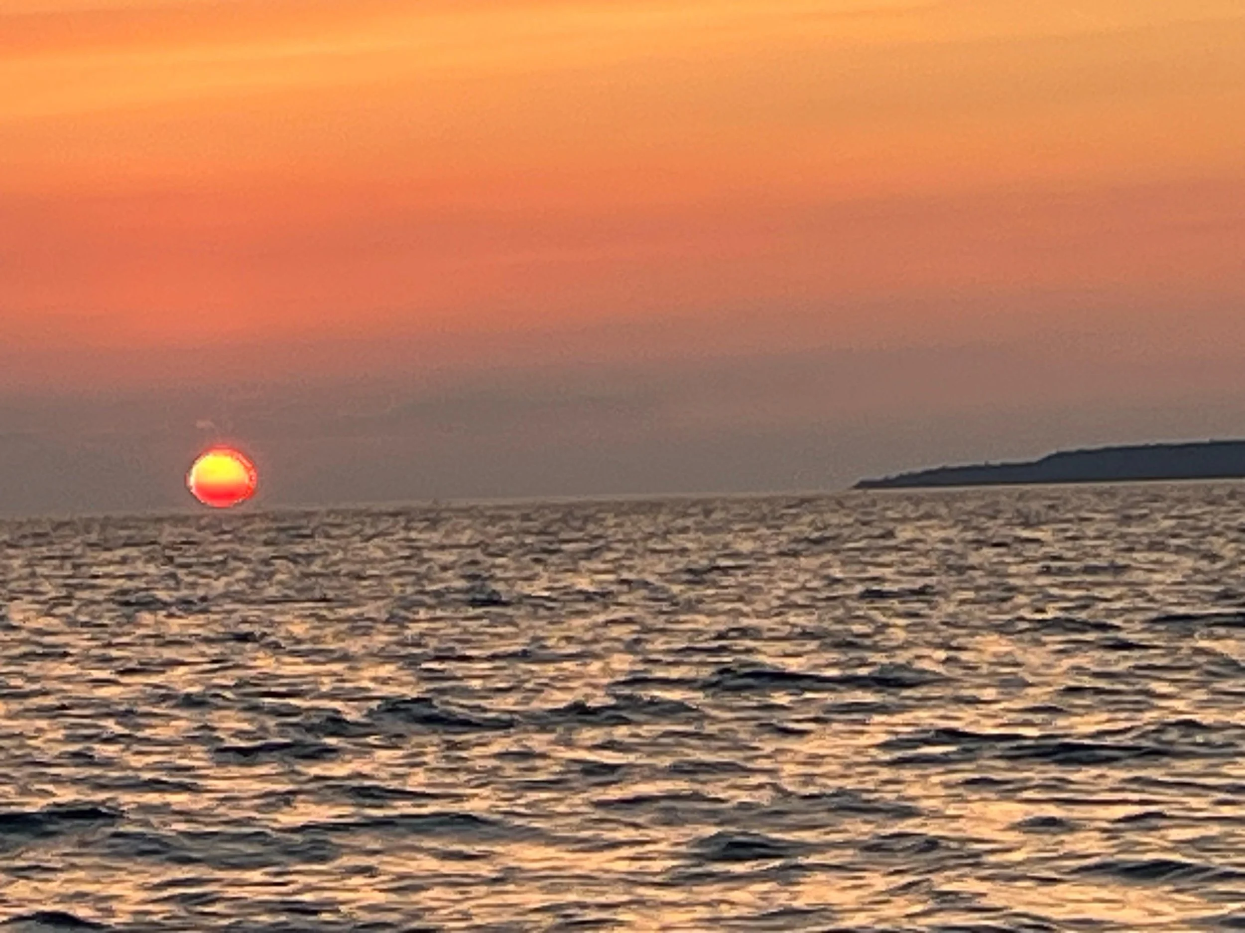 Sunset over a body of water with the sun near the horizon and some distant land or mountains.