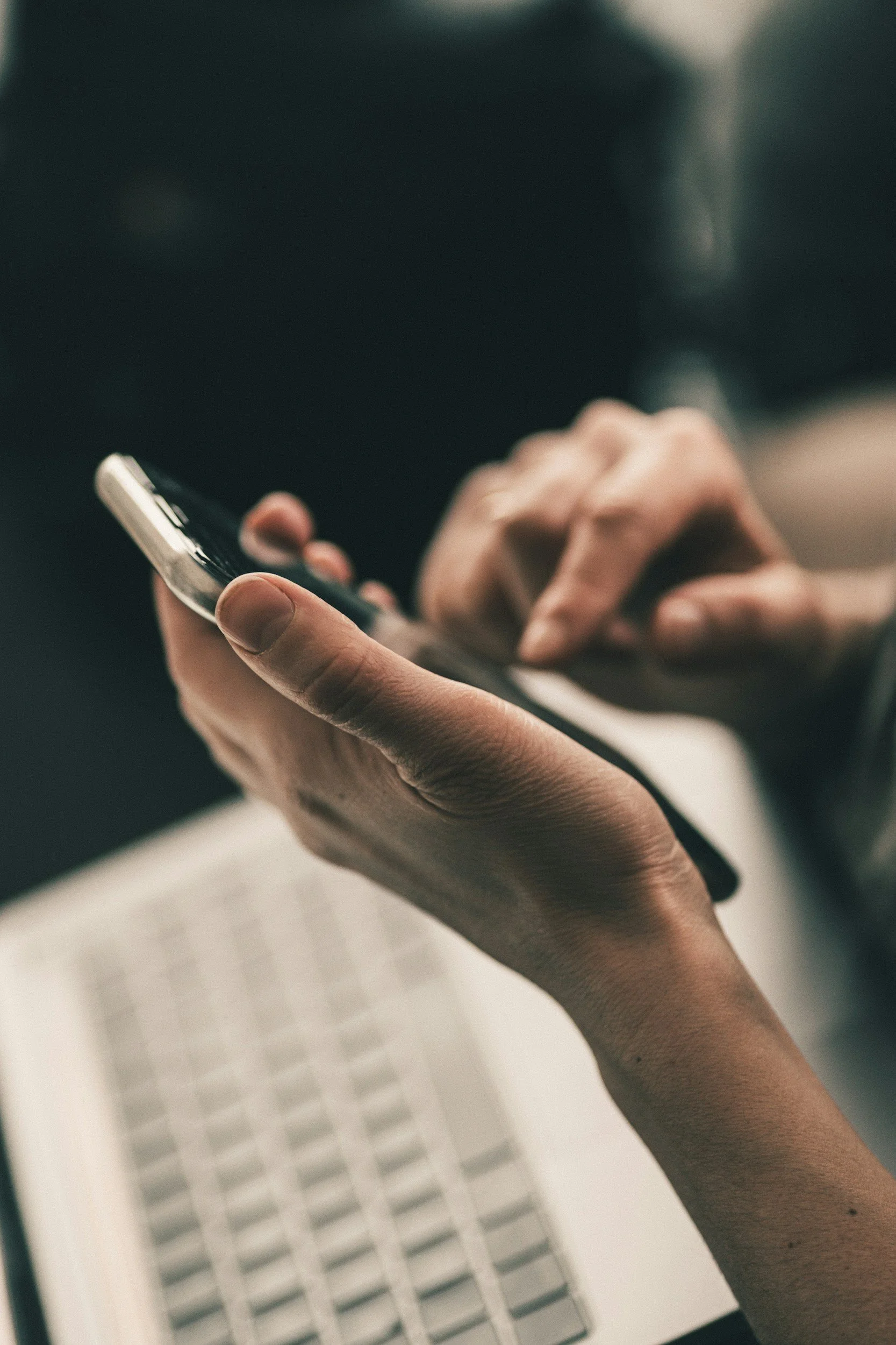 Close-up of a person's hand holding a smartphone, with a blurred background showing a white lattice or grid pattern.