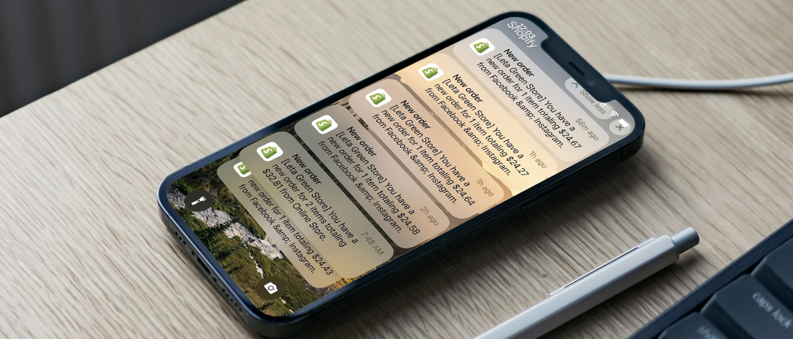 Close-up of an iPhone on a wooden desk showing multiple Facebook notification messages about new orders, with a pen nearby.