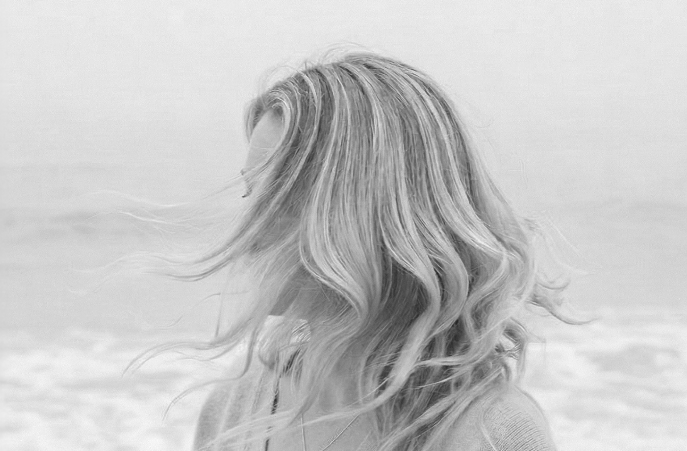 Black and white photograph of a woman with long, flowing hair turned away from the camera against a plain background.
